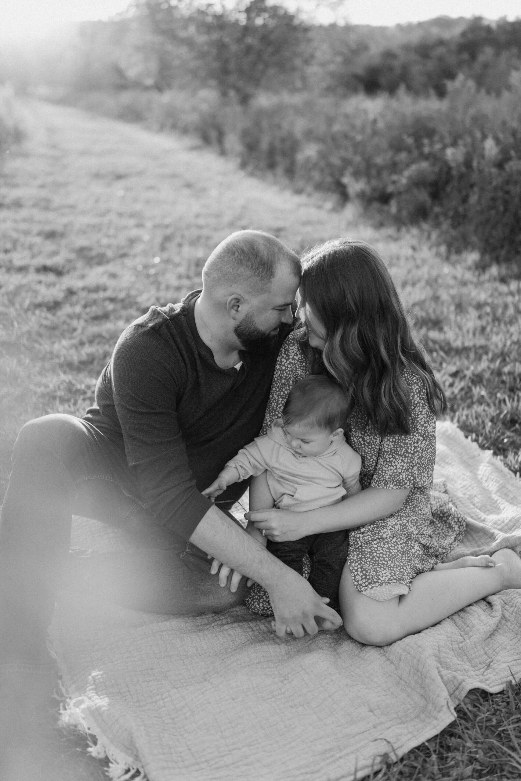 a family (father, mother, and son) sitting and embracing on a picnic blanket at Peace Valley Park