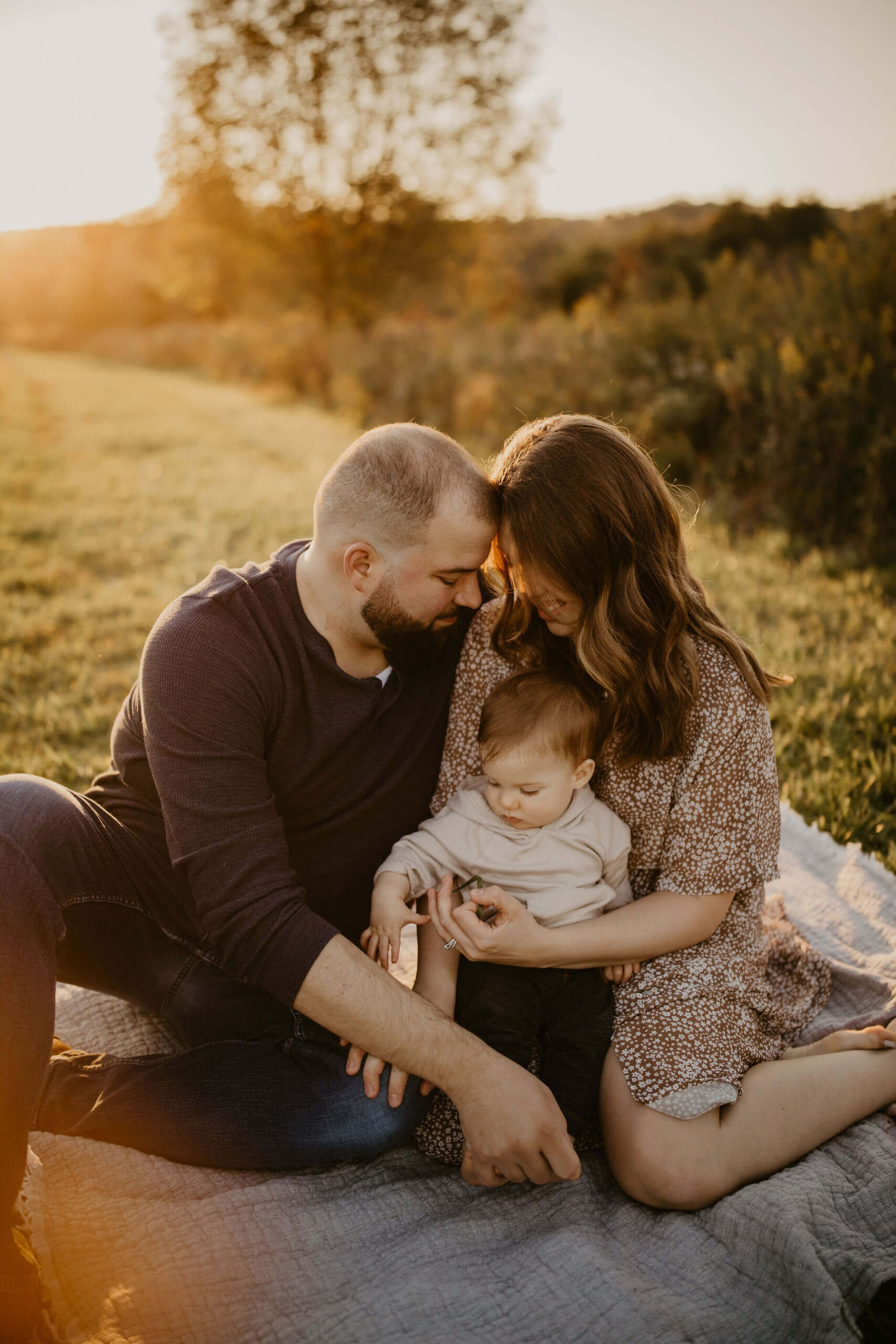 a family (father, mother, and son) sitting and embracing on a picnic blanket during a family session