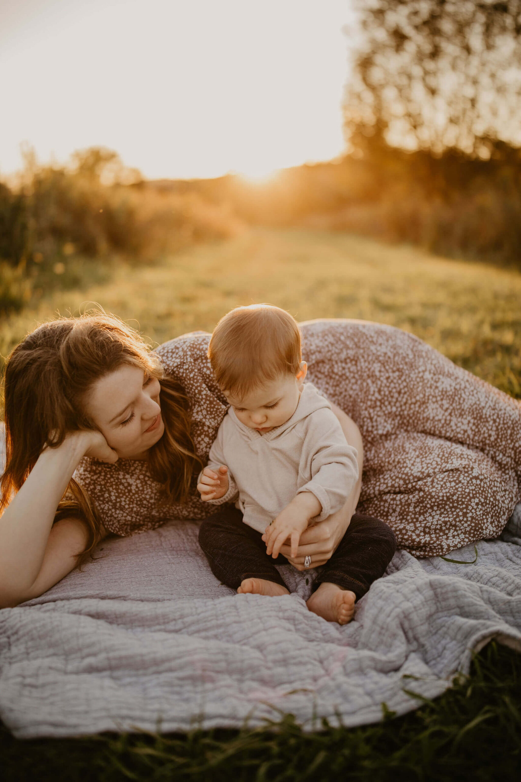 a mother and her son laying on a picnic blanket in a field at sunset in Peace Valley Park