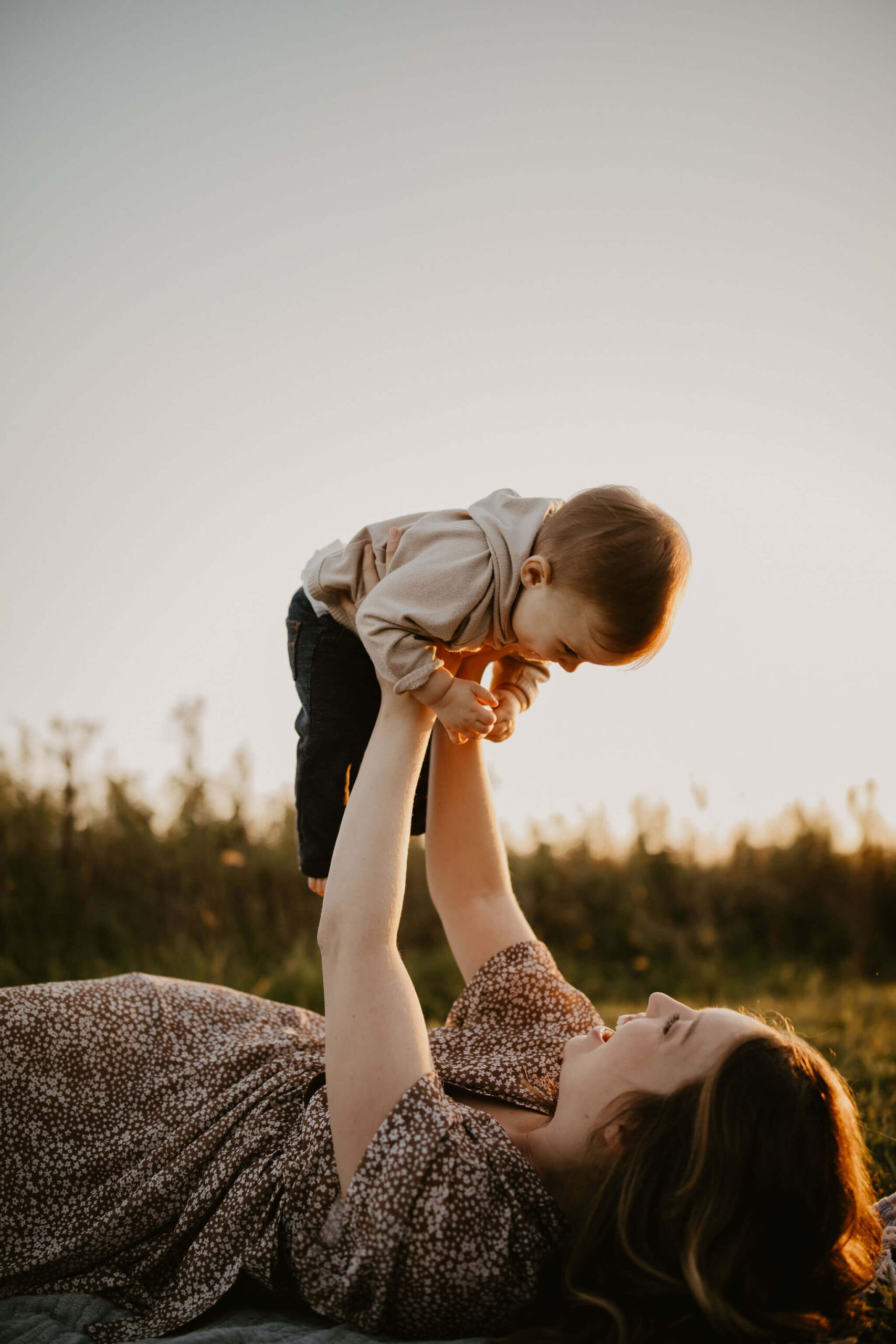 a mother lifting her son in the air, laying on the ground and smiling at each other in Pennsylvania
