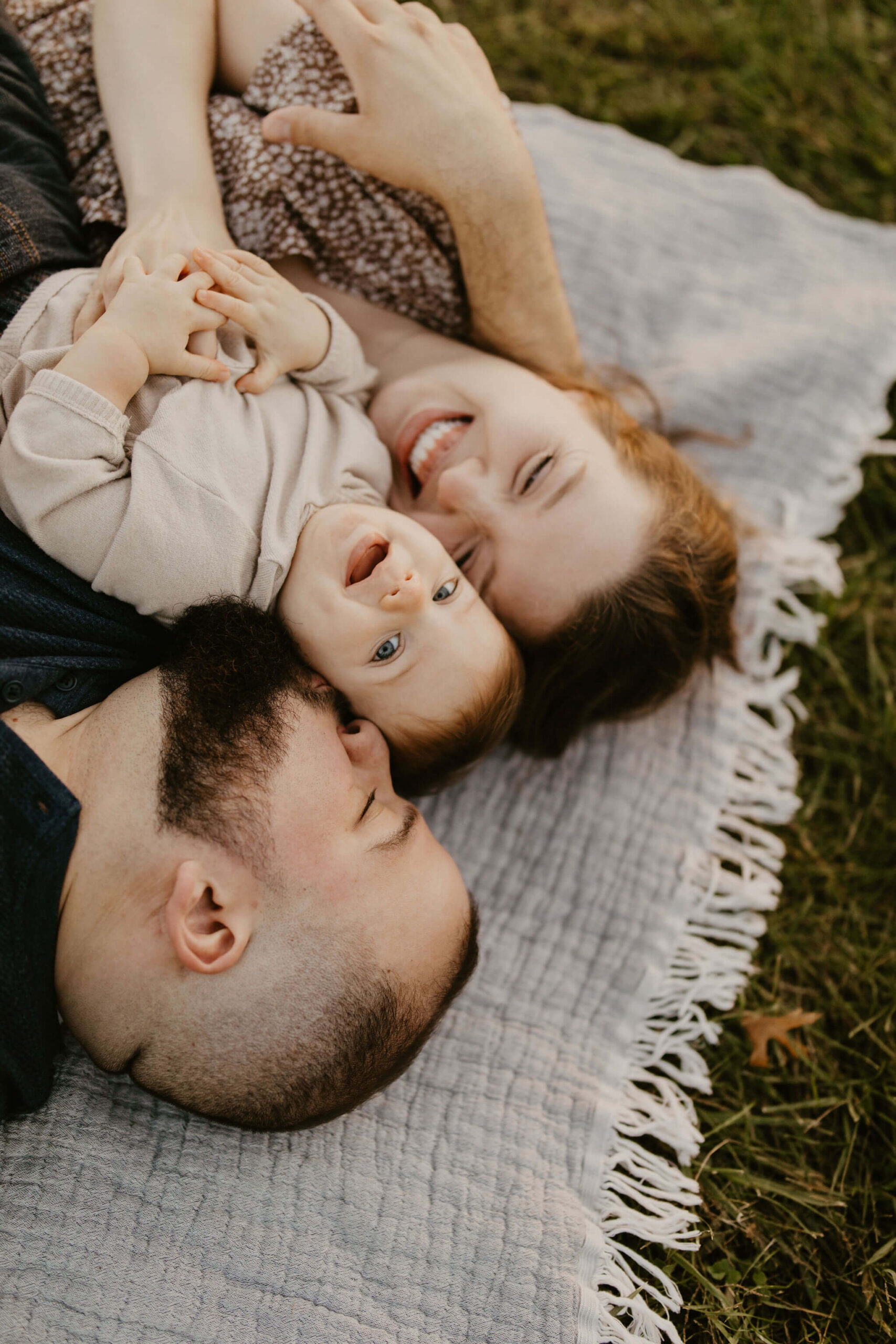a family (father, mother, son) laying on a picnic blanket, cuddling together and laughing during a family session
