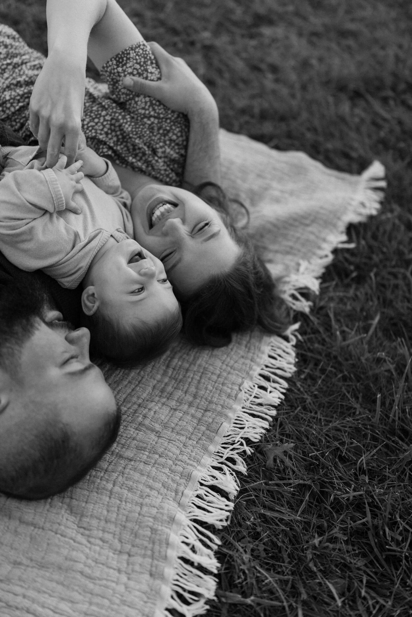 a family (father, mother, son) laying on a picnic blanket, cuddling together and laughing during a family session