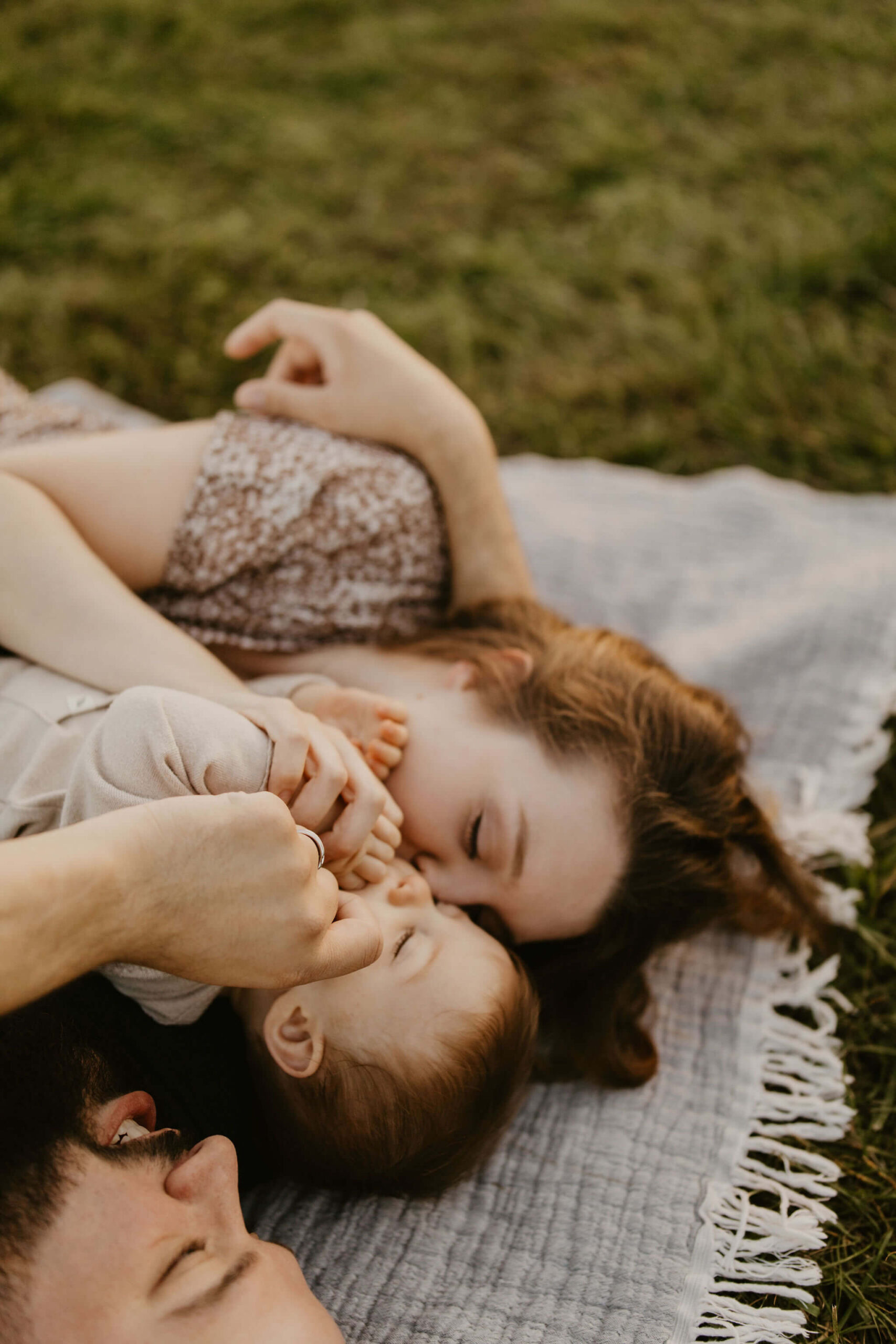 a family (father, mother, son) laying on a picnic blanket, cuddling together and laughing during a family session