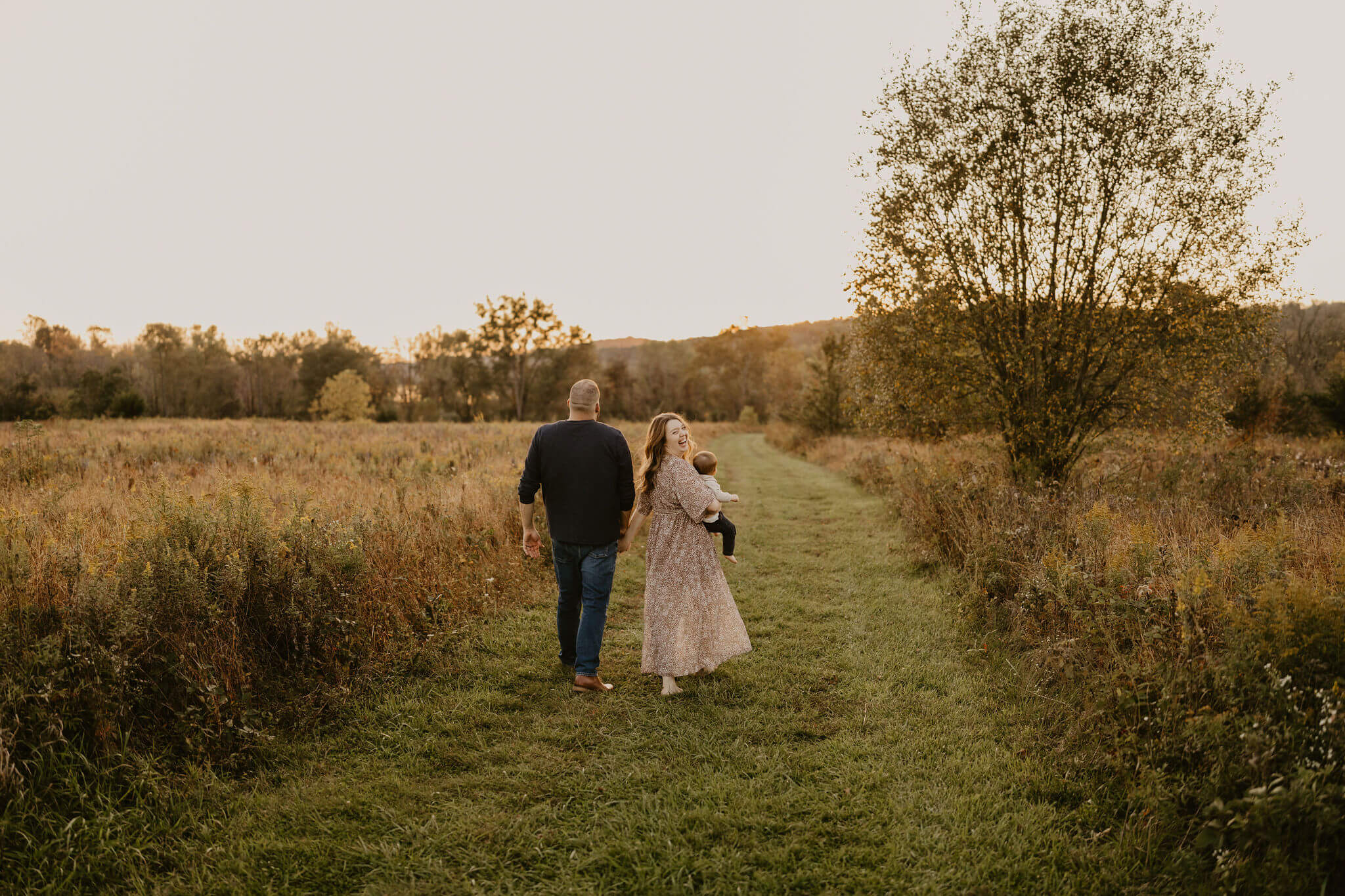 a family (father, mother, and son) walking away from the camera toward the sunset in a field during fall at Peace Valley Park