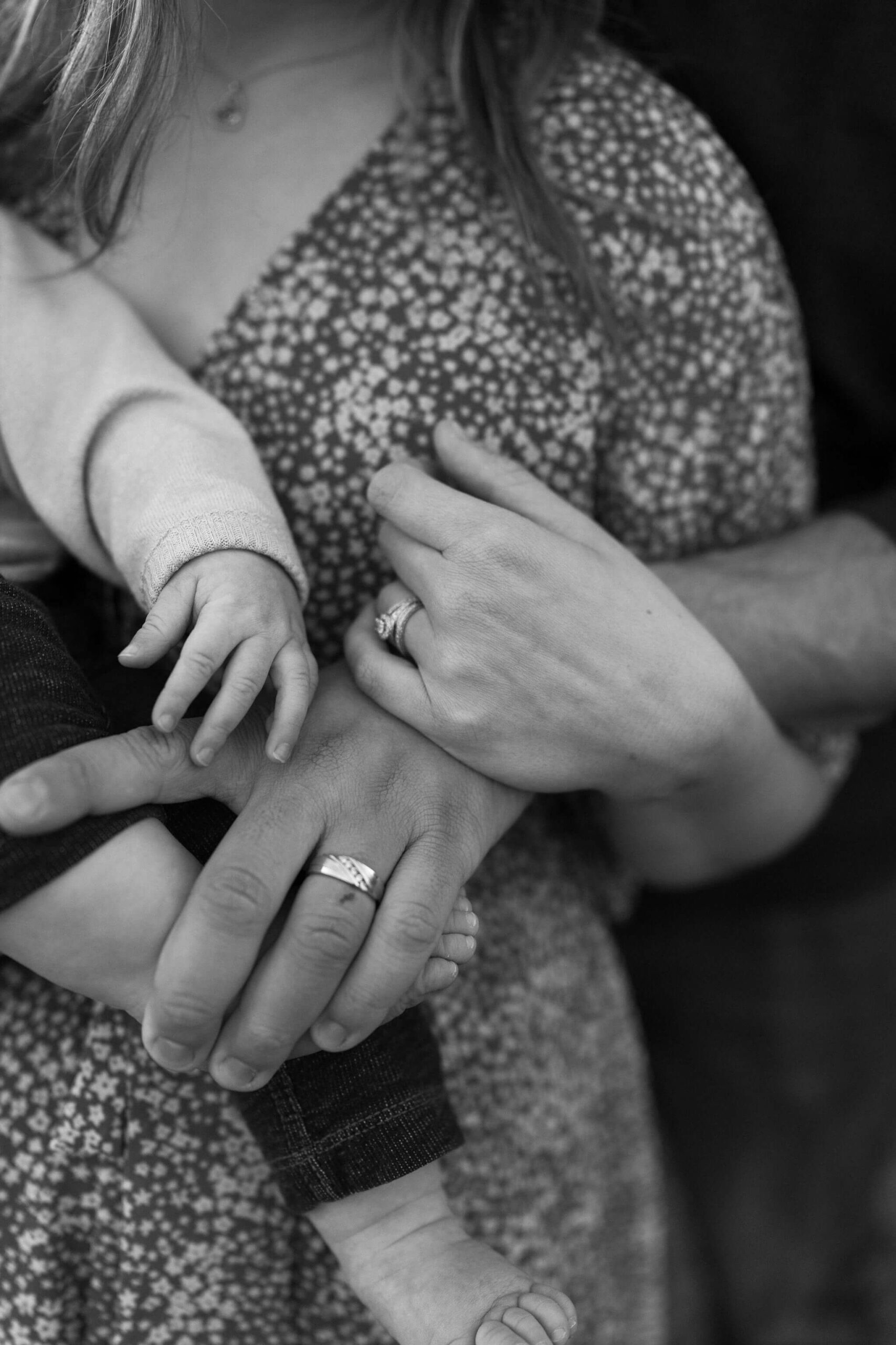 black and white close up image of hands: a mother and father, both with their wedding rings, and their young son at their family session