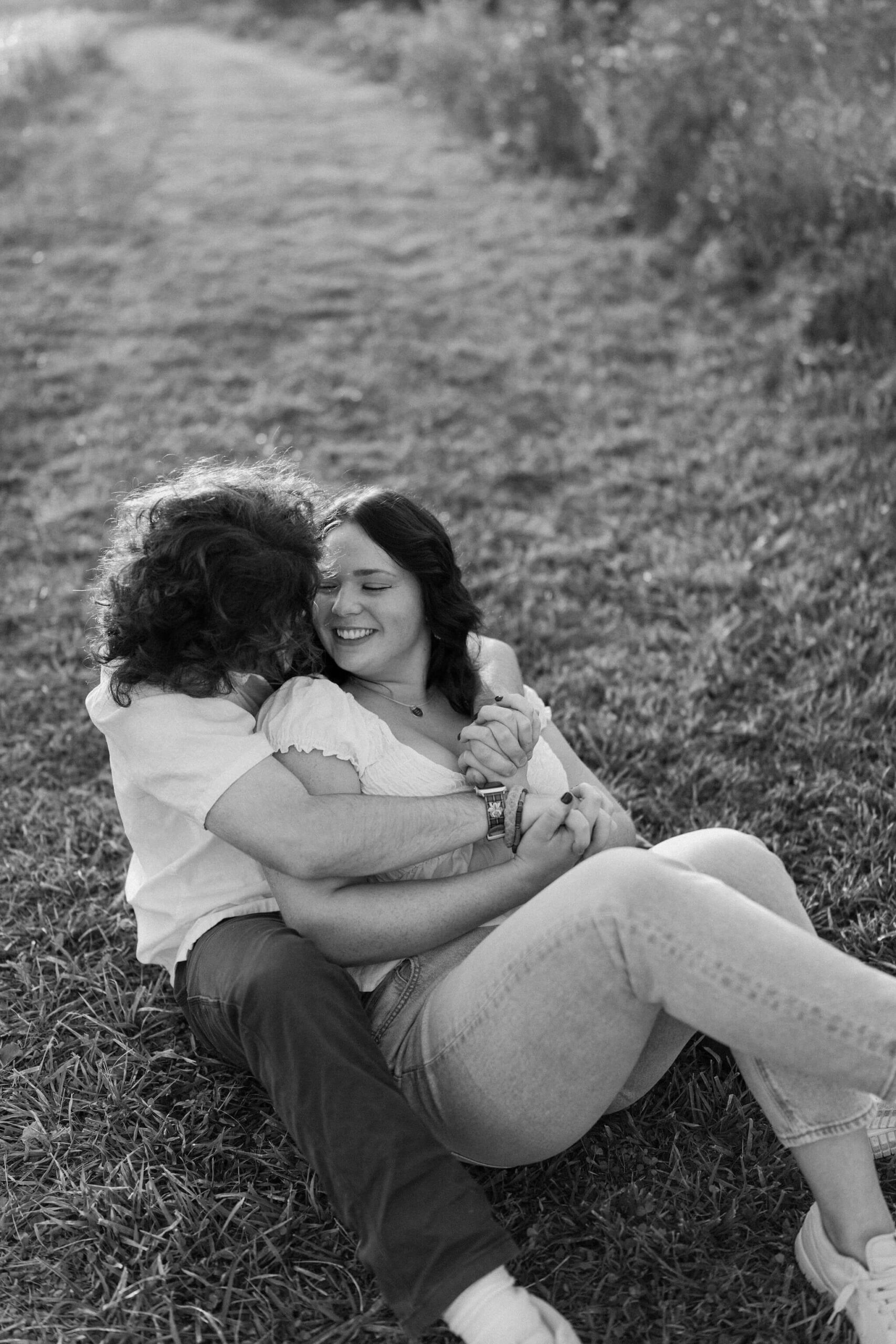 black and white image of a couple cuddling in a field, laughing, in doylestown pa