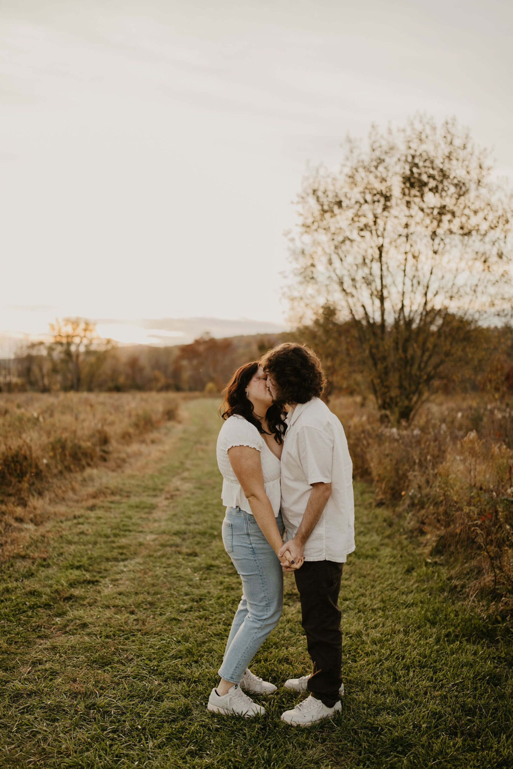 a young couple holding hands and kissing in a golden field at sunset in doylestown pa