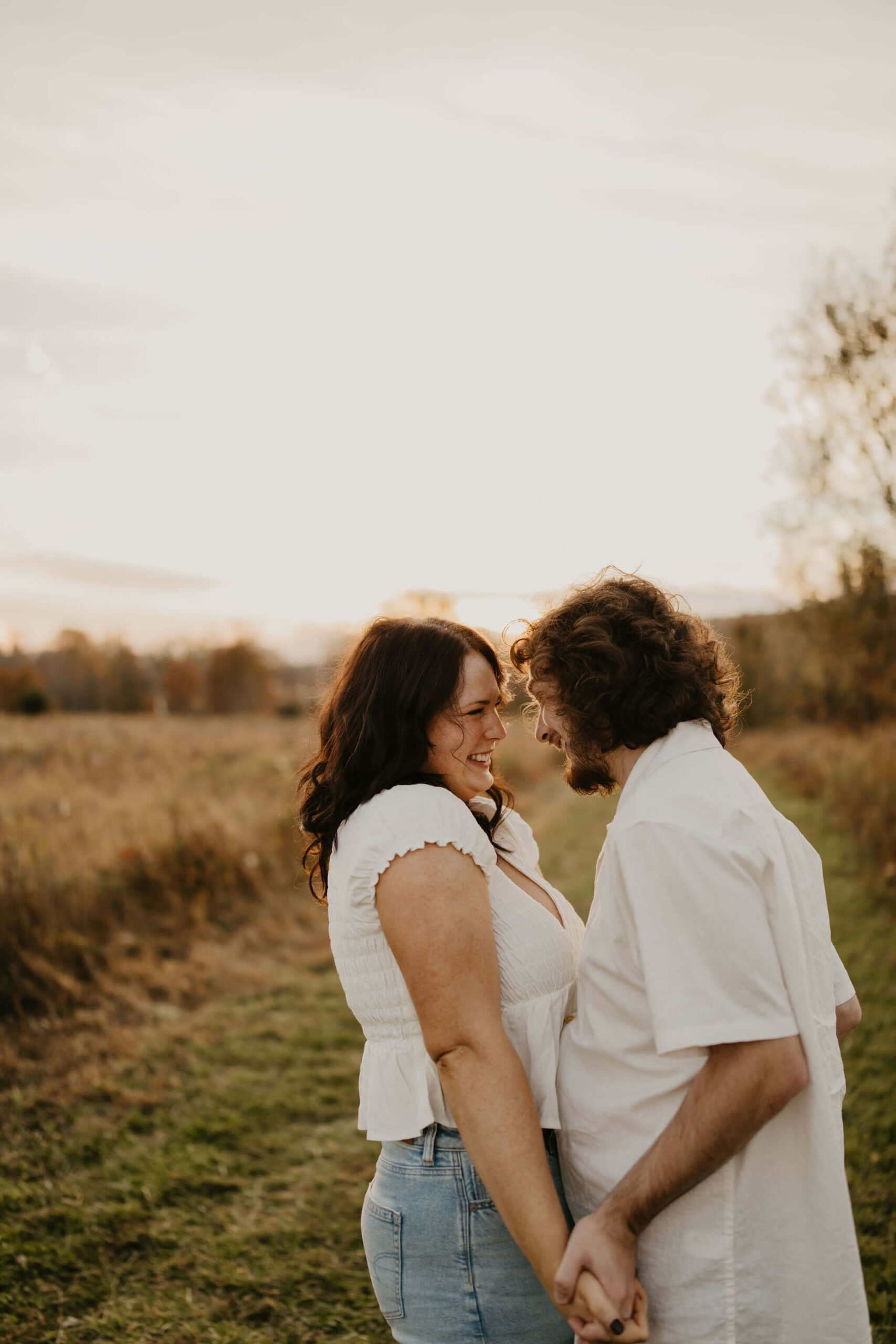 a boy and a girl holding hands in a field and smiling at each other during their couples session