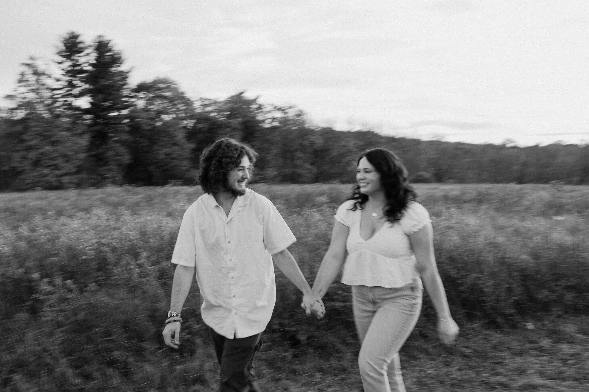 a motion-blur black and white image of a couple walking through a field, smiling at each other during a couples session