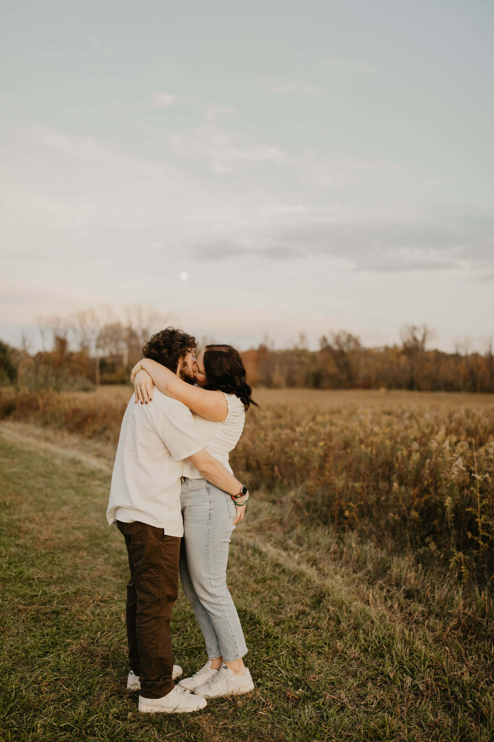 a young couple kissing in a field at sunset while the moon rises over them in doylestown pa