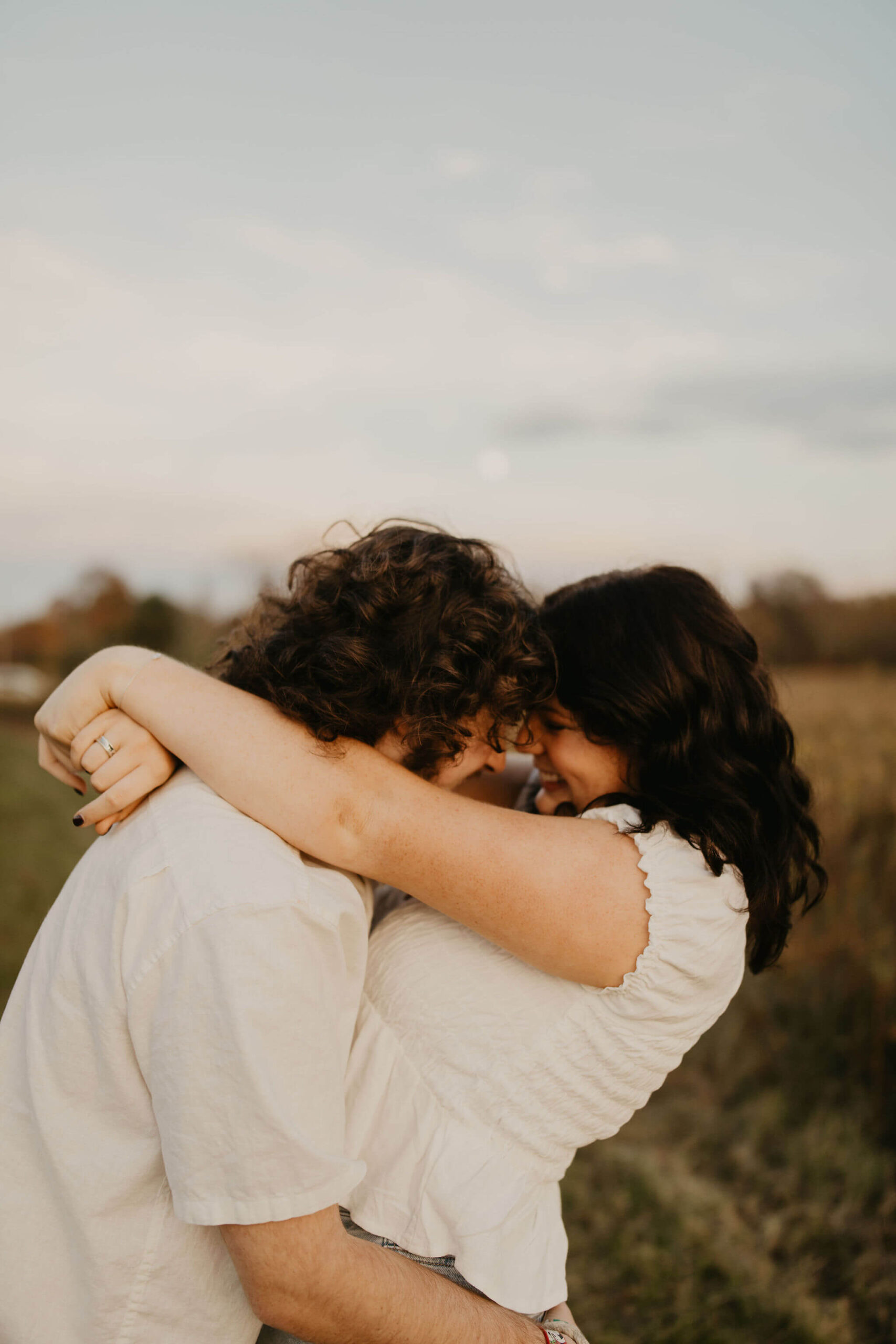 a boy and a girl embracing and giggling in a field at sunset in doylestown
