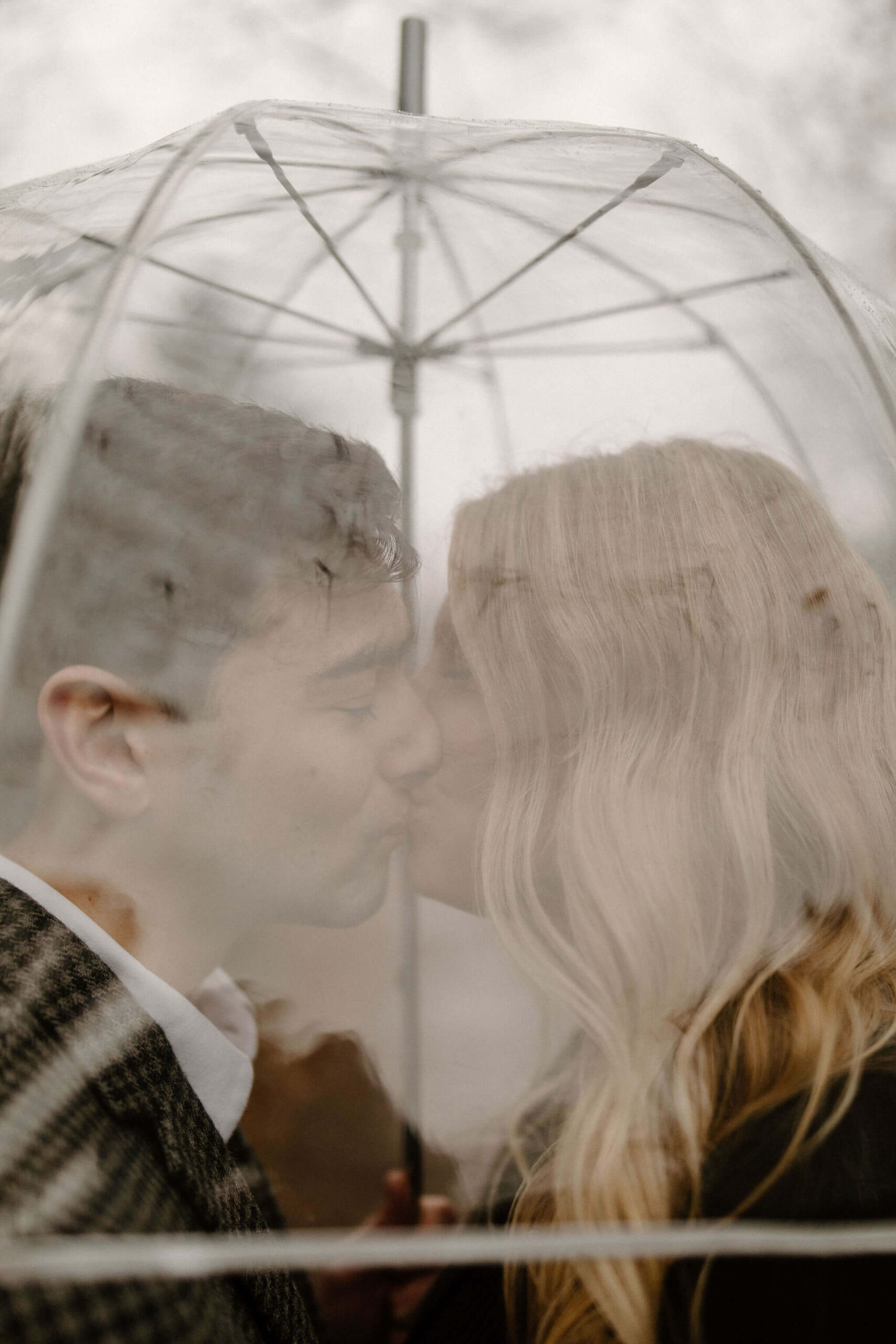 close up image through a clear umbrella of a man and woman kissing inside the umbrella during their engagement session