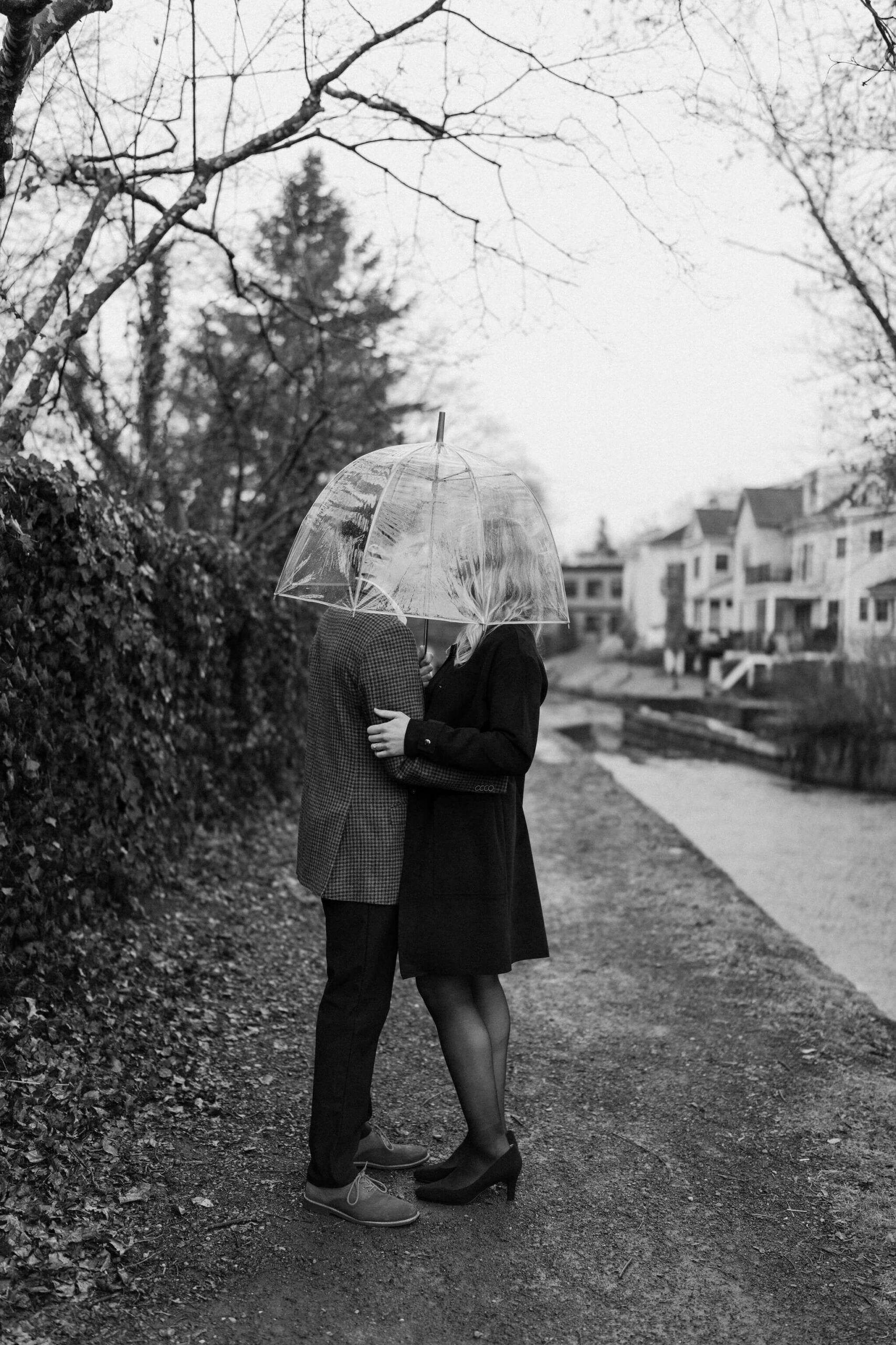 black and white image of a man and woman holding each other, with a clear umbrella held over their heads and obscuring the view of their faces in New Hope