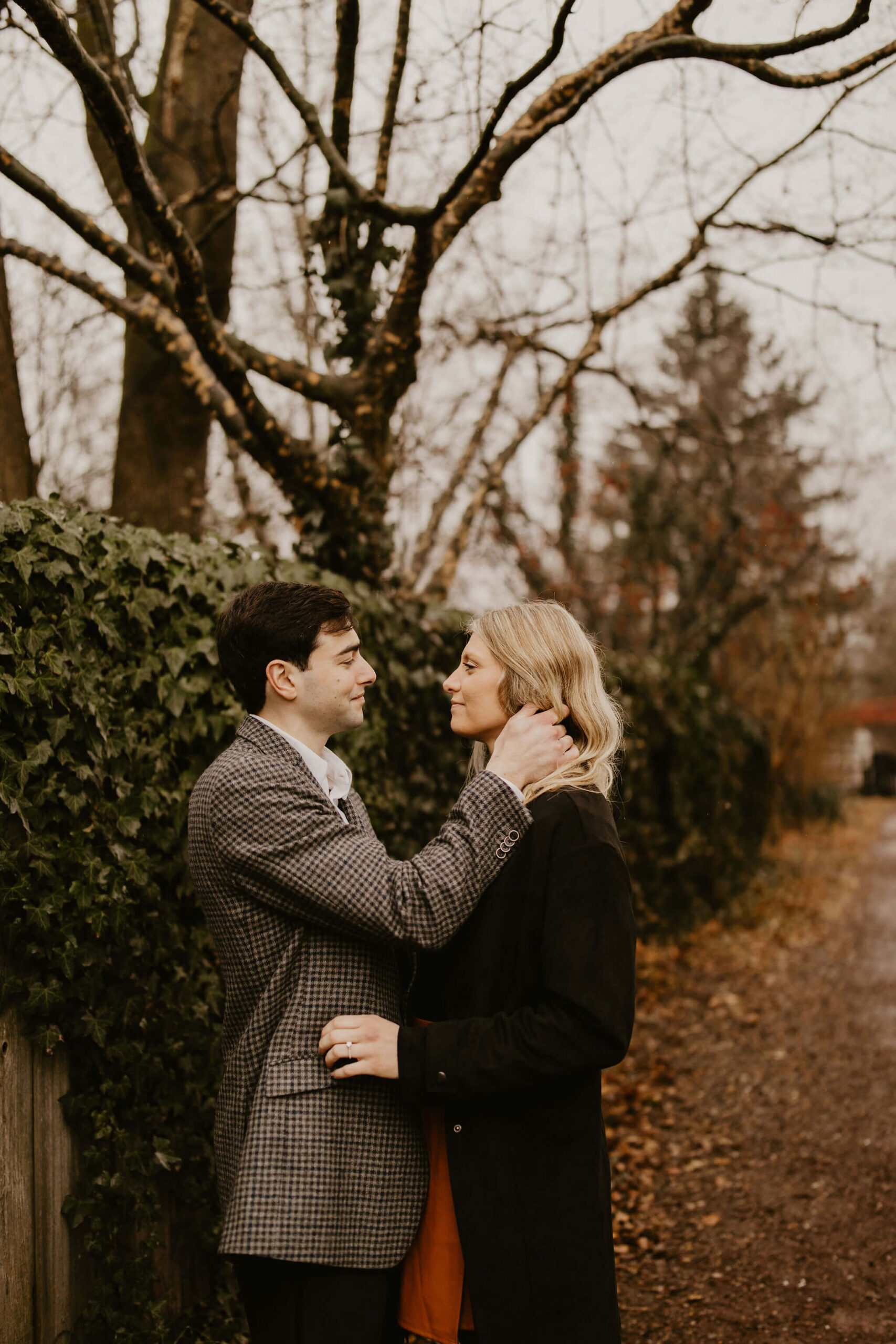man pushing a woman's blonde hair behind her ear, looking at each other and smiling softly during their engagement session in New Hope