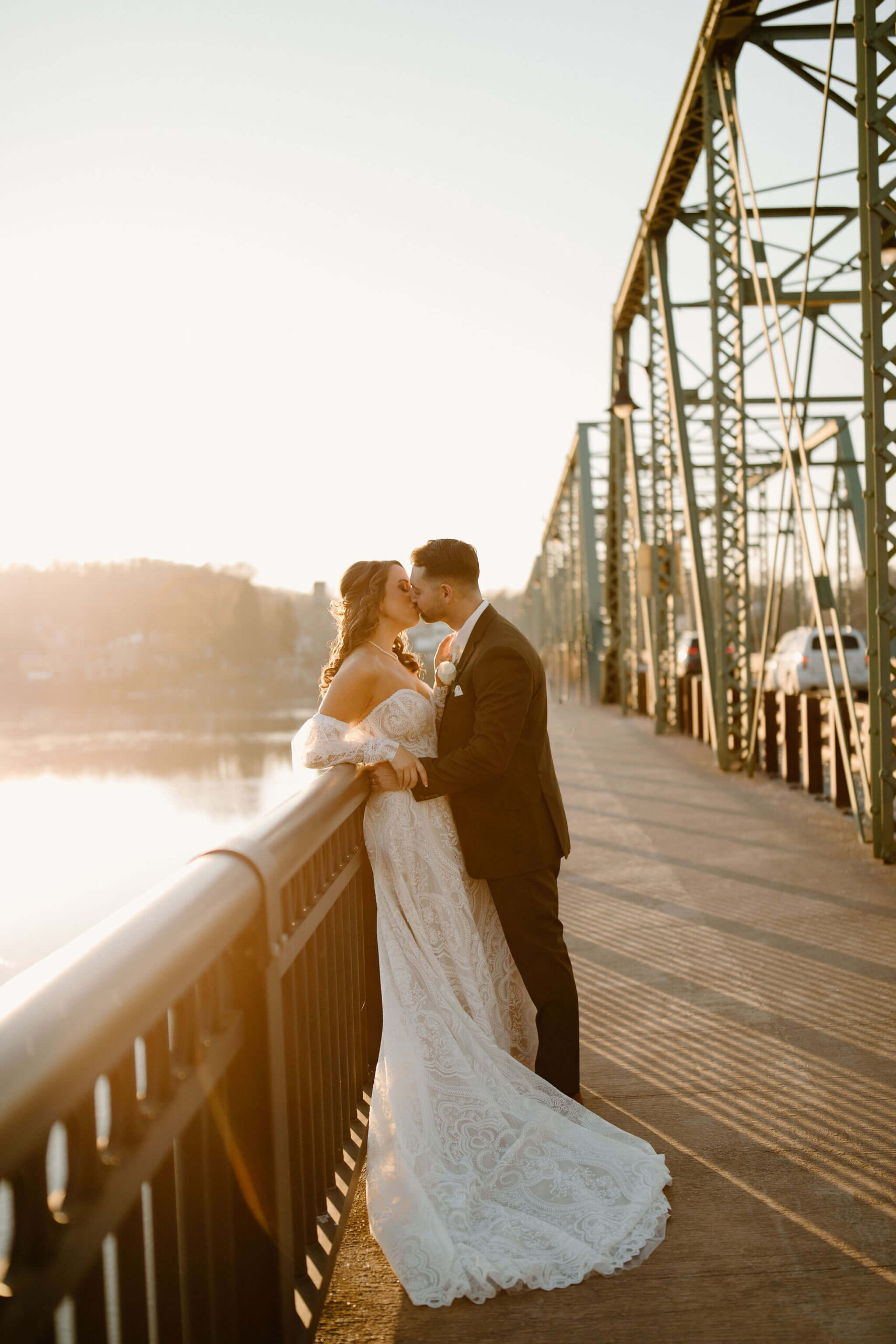 Bride and Groom kissing on a bridge at sunset, overlooking the river on their new jersey wedding day