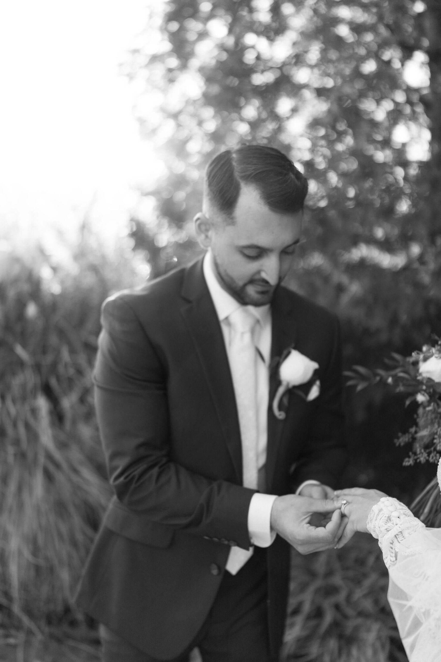 black and white image of a groom straightening his bride's engagement ring on her finger in lambertville new jersey