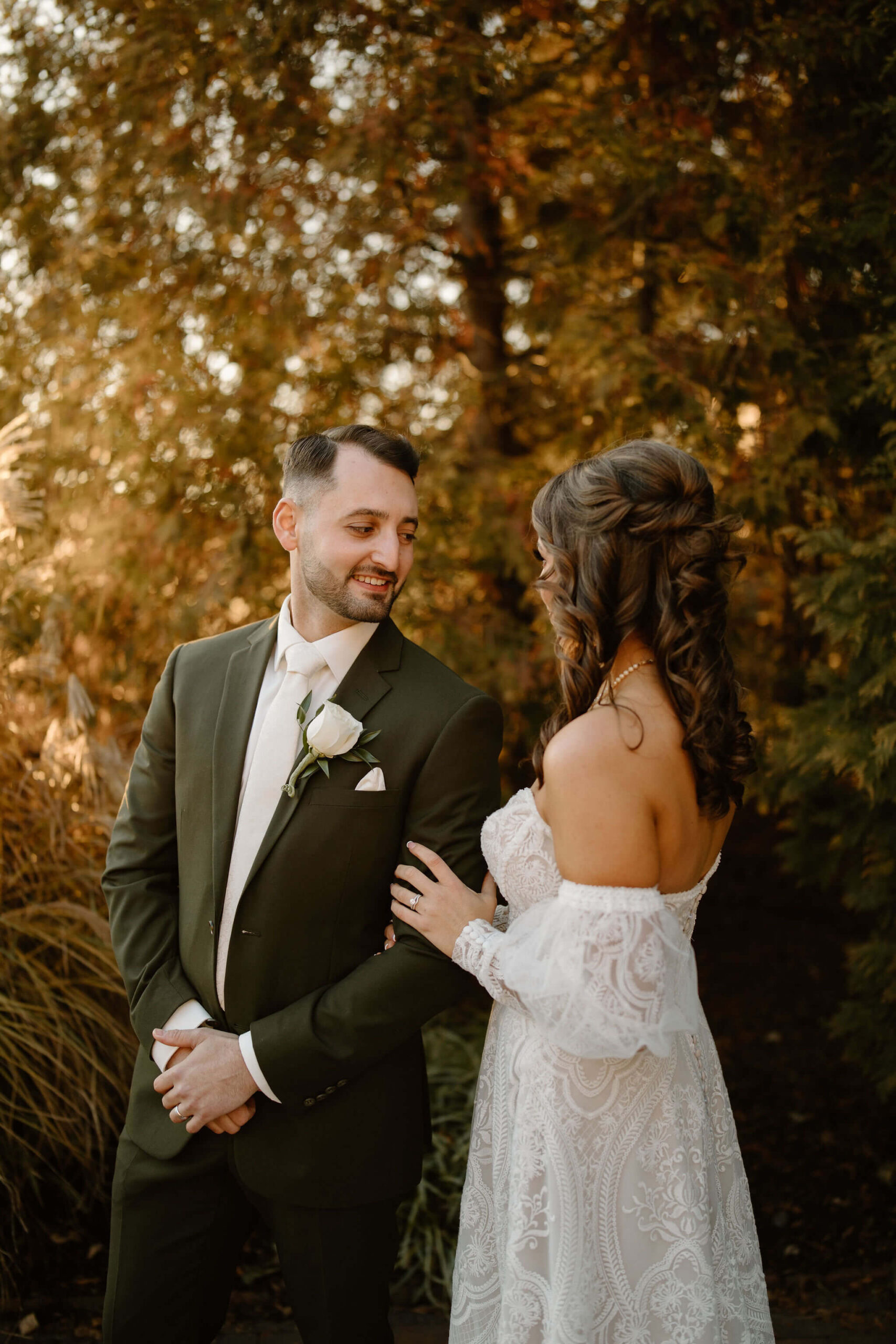 bride (brown hair, textured dress) and groom (brown hair, dark green suit) smiling at each other on their wedding day