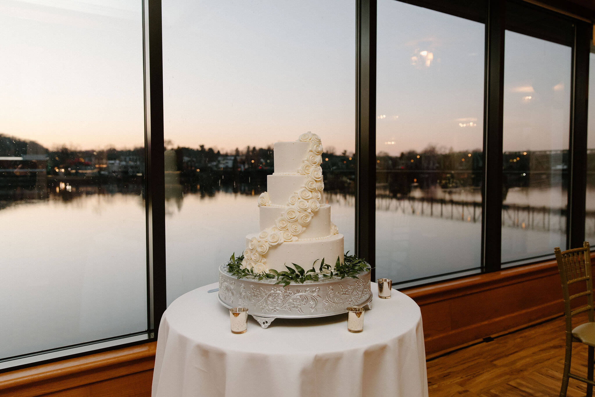 four-tiered white wedding cake, with a thick band of white roses wrapping around the cake from top-to-bottom, with the sun setting out the window behind it in lambertville new jersey