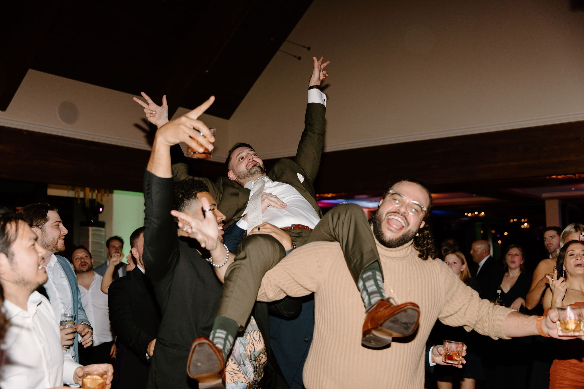 groom (green suit) waving his hands in the air as his friends lift him on their shoulders, all smiling and cheering in lambertville new jersey