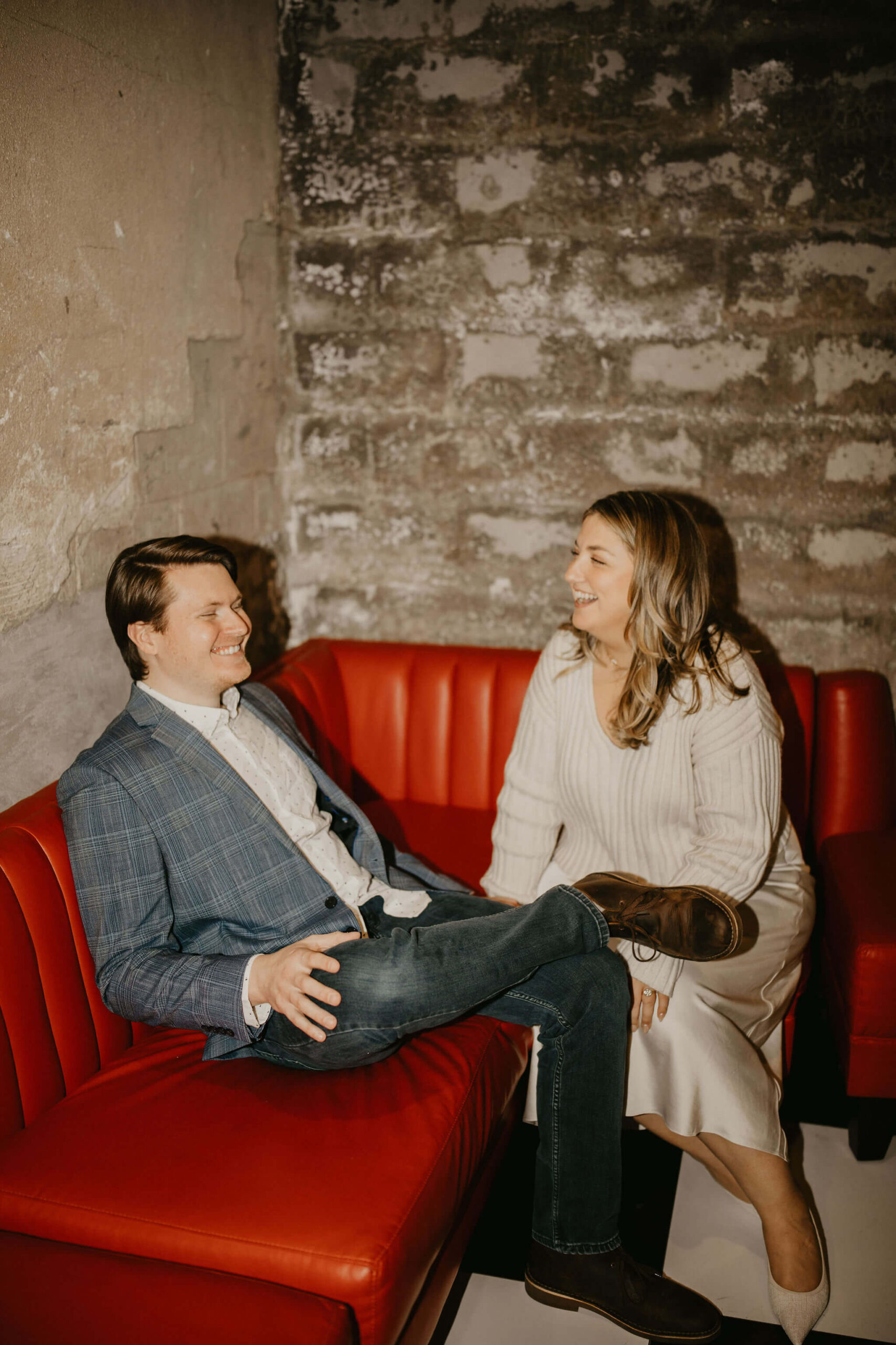 a couple sitting on a red leather couch, leaning toward each other and laughing at the Logan Inn