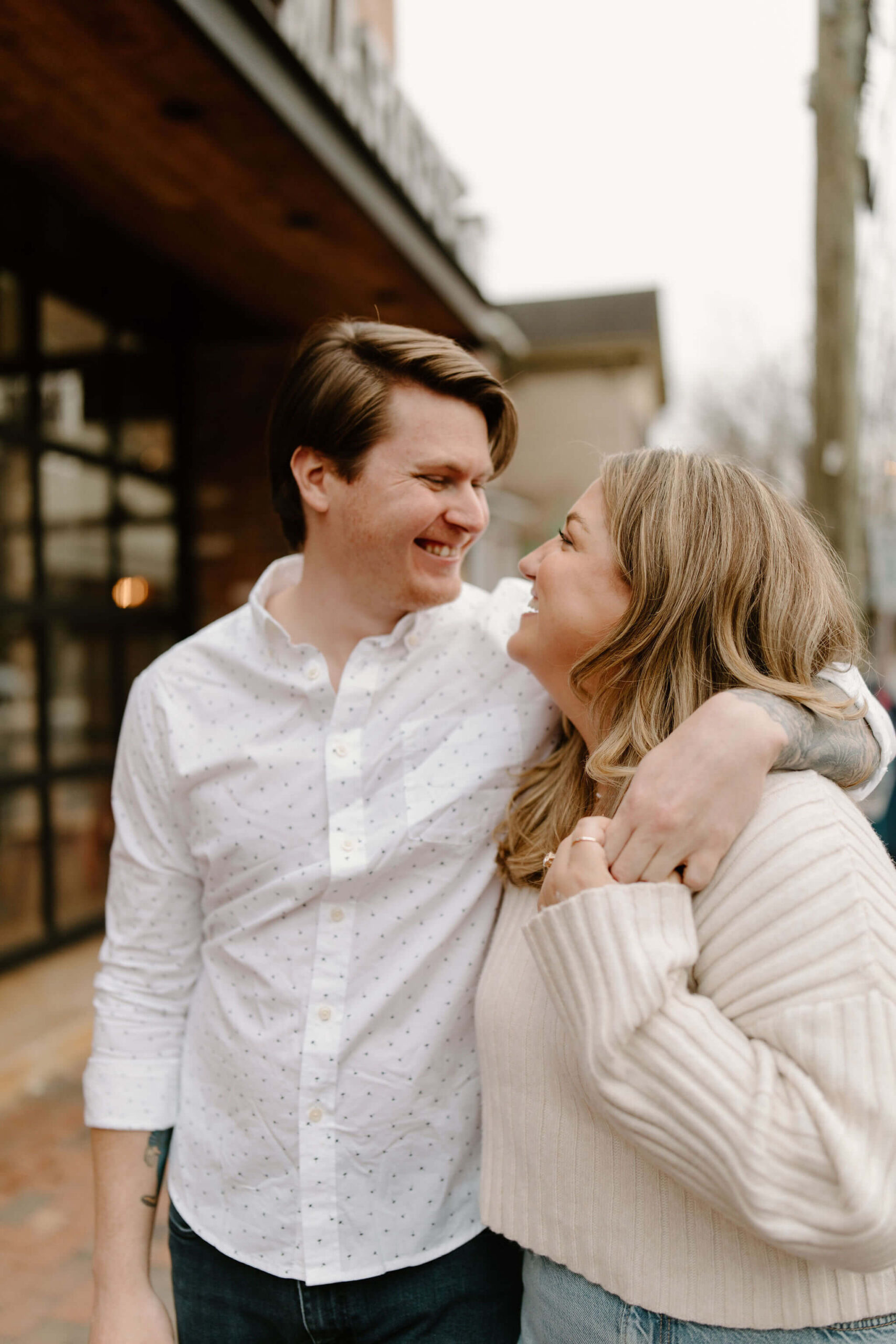 man with his arm around a woman's shoulders, laughing at each other, taking engagement photos in New Hope, Pennsylvania