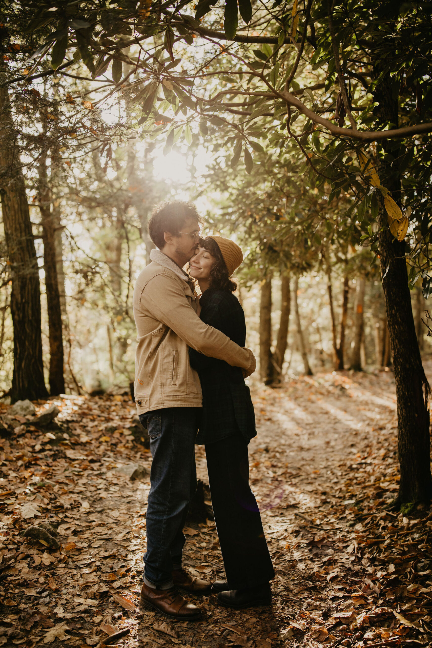 engagement session photo of a man and a woman on a hiking trail, embracing while he kisses her forehead