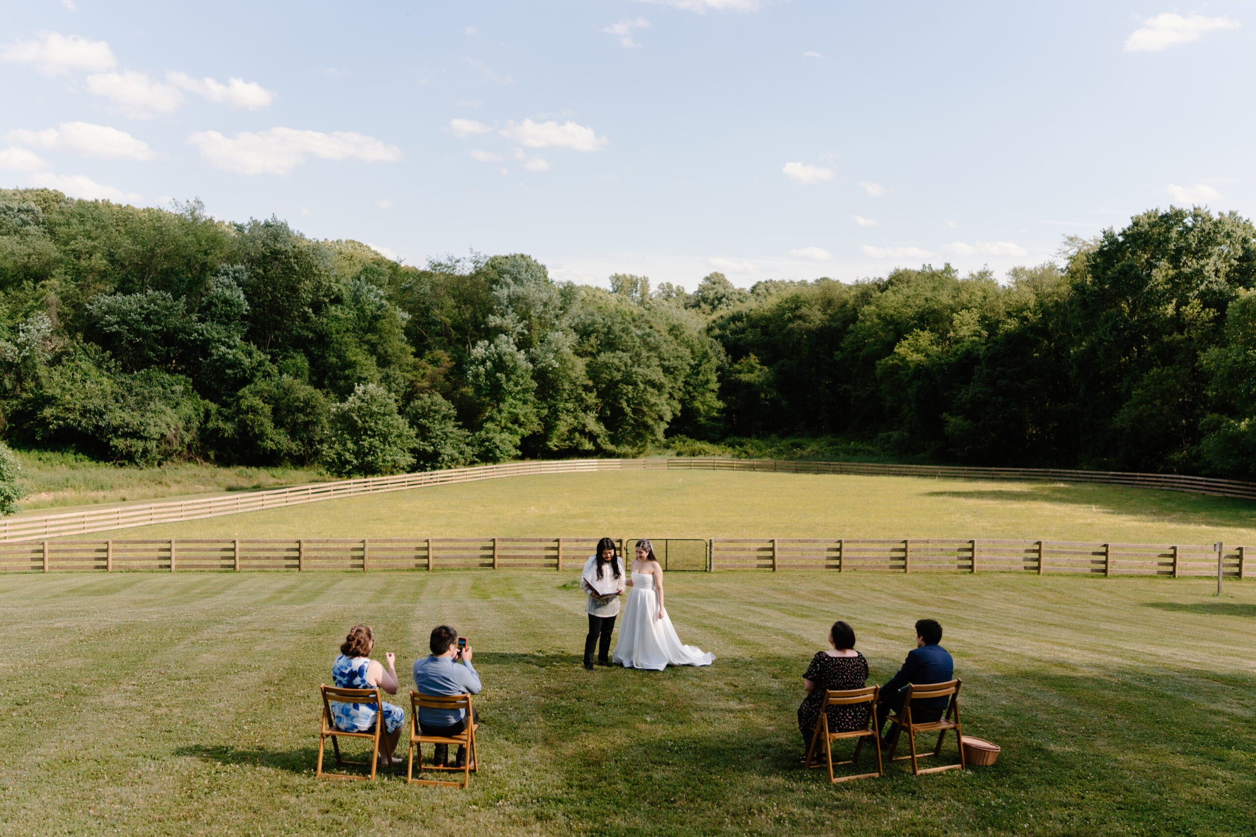 bride and groom exchanging vows in a meadow, with four of their closest friends sitting and watching their alternative wedding day