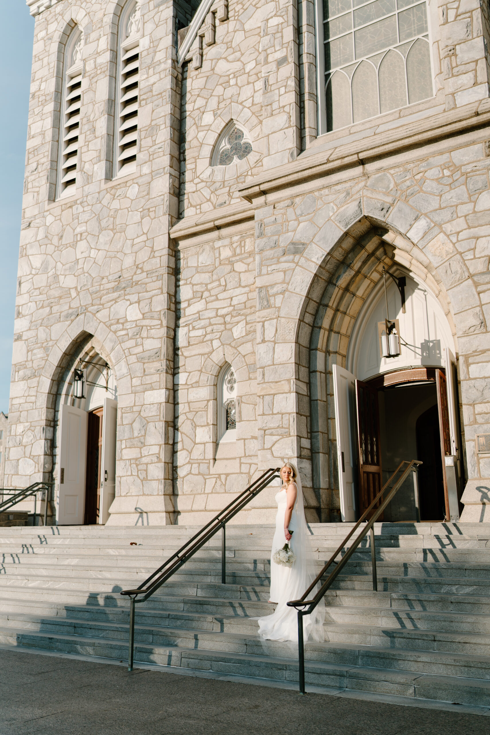photograph of bride before her wedding standing on steps to Villanova cathedral, looking over her shoulder and holding her bouquet down at her side