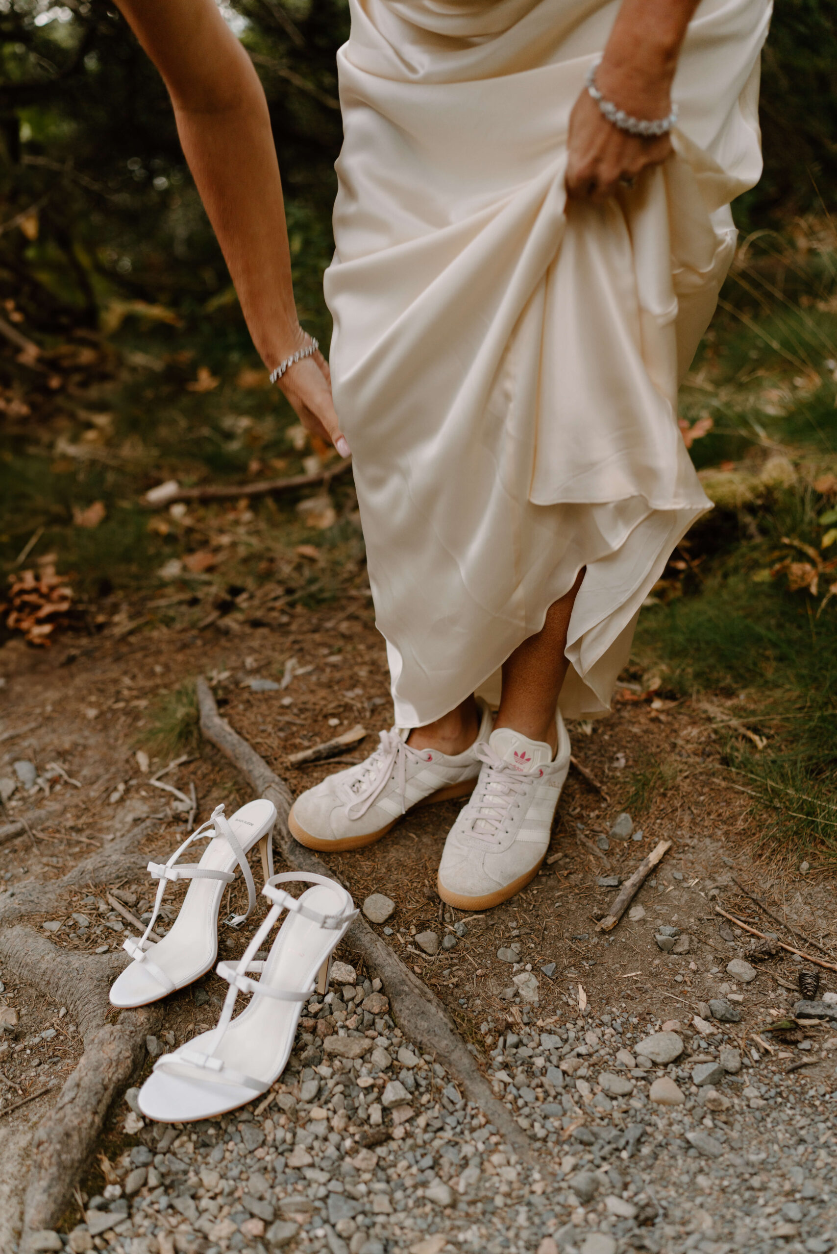 close up image of a bride bending down and lifting her skirt to change from her white sneakers into her white stiletto heels before her elopement