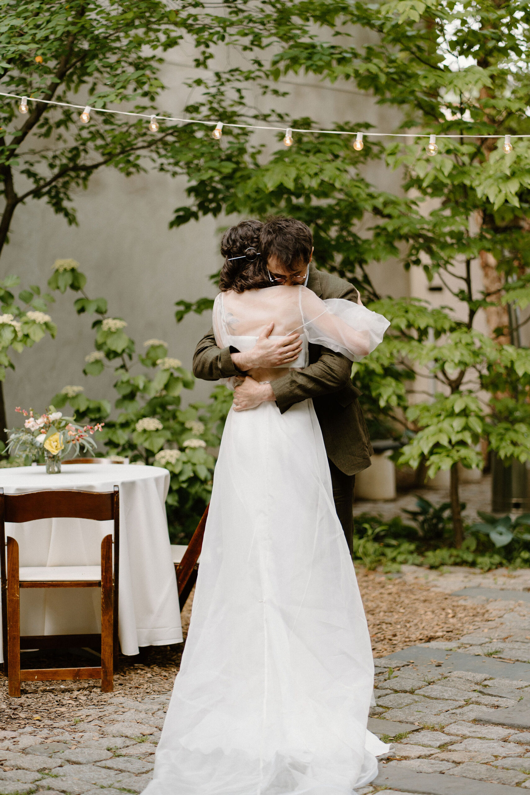 bride and groom embracing after their wedding ceremony, away from their guests, in a lush green cobblestone courtyard during their spring wedding at the Maas Building