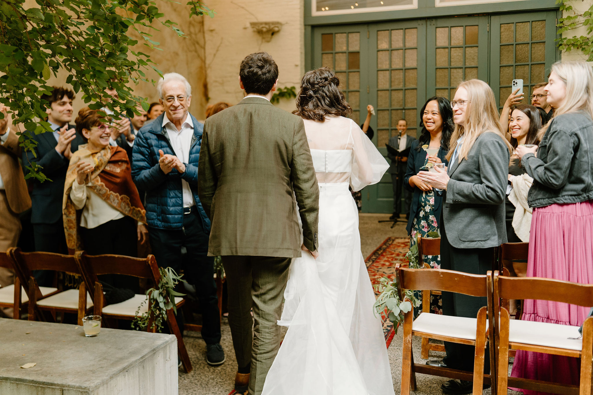 bride and groom entering their ceremony aisle together at the Maas Building, while their guests smile at them