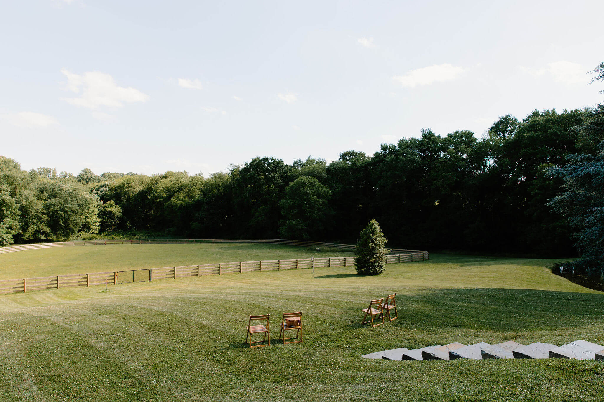 four wooden chairs placed in an open field for an elopement ceremony, with a rolling hill and forest in the background. A large fence cuts through the middle of the field