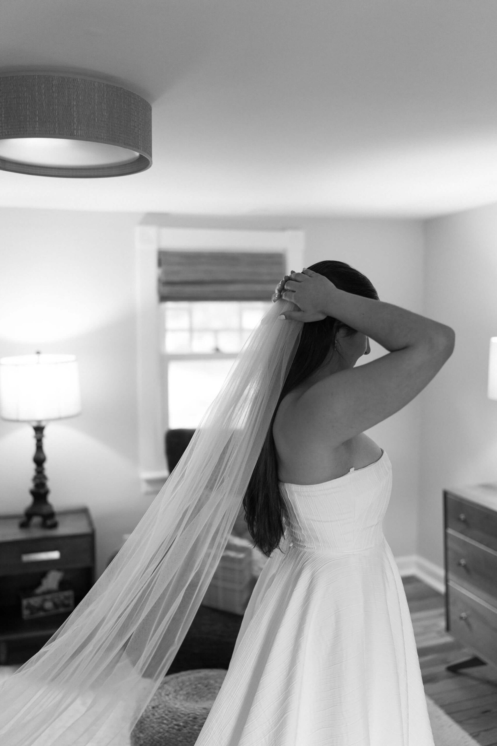 black and white image of bride pressing veil into her long brown hair, wearing strapless wedding gown as she gets ready for her pennsylvania elopement