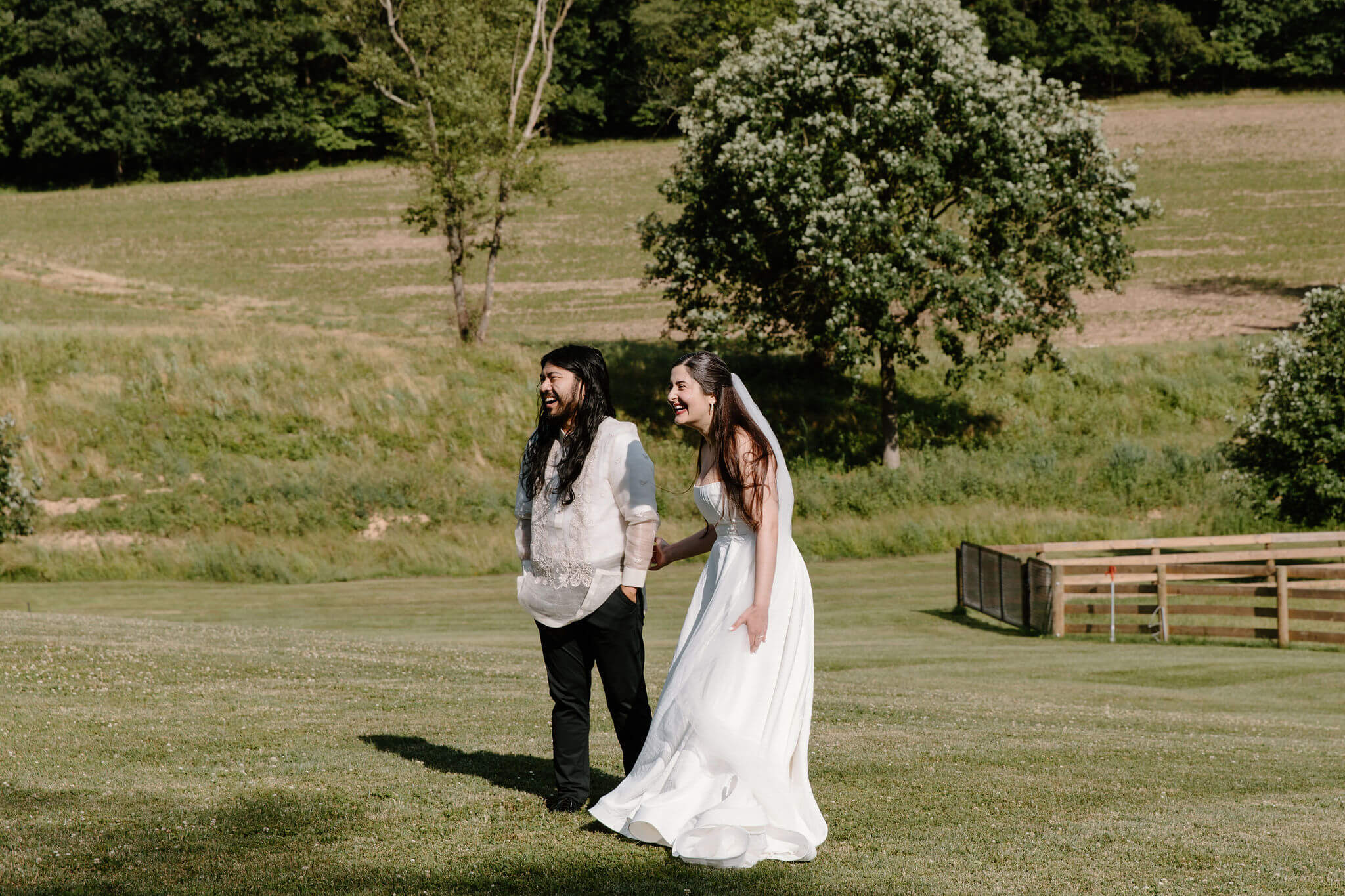 bride and groom holding hands and laughing toward their guests during their elopement ceremony, standing in a grassy field at a farmhouse in Pennsylvania
