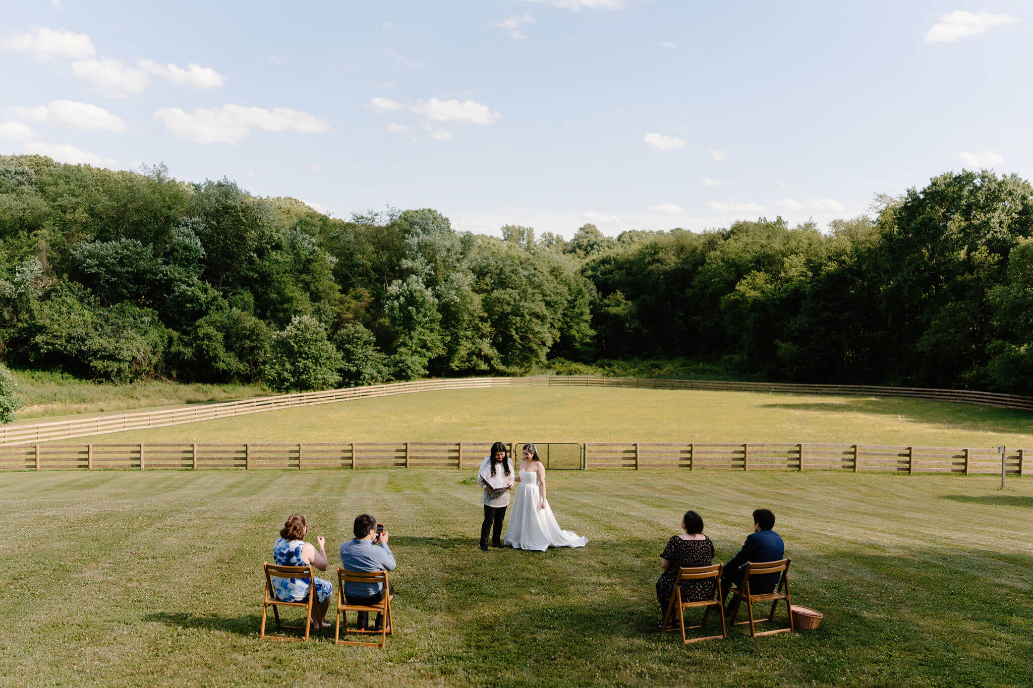 bride and groom standing in their self uniting elopement ceremony in Pennsylvania, reading out of a binder to the four friends witnessing their marriage, in an open field on a sunny day