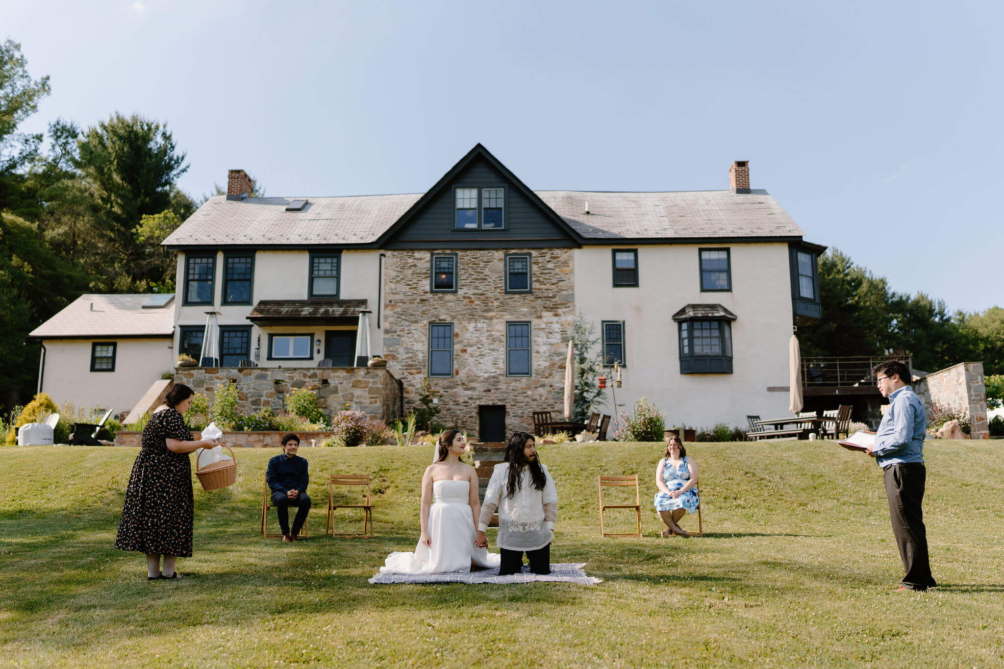 bride and groom kneeling on a blanket during their elopement ceremony, two guests seated behind them, with one guest standing on either side of them to perform a Filipino ceremony at a farmhouse in Pennsylvania
