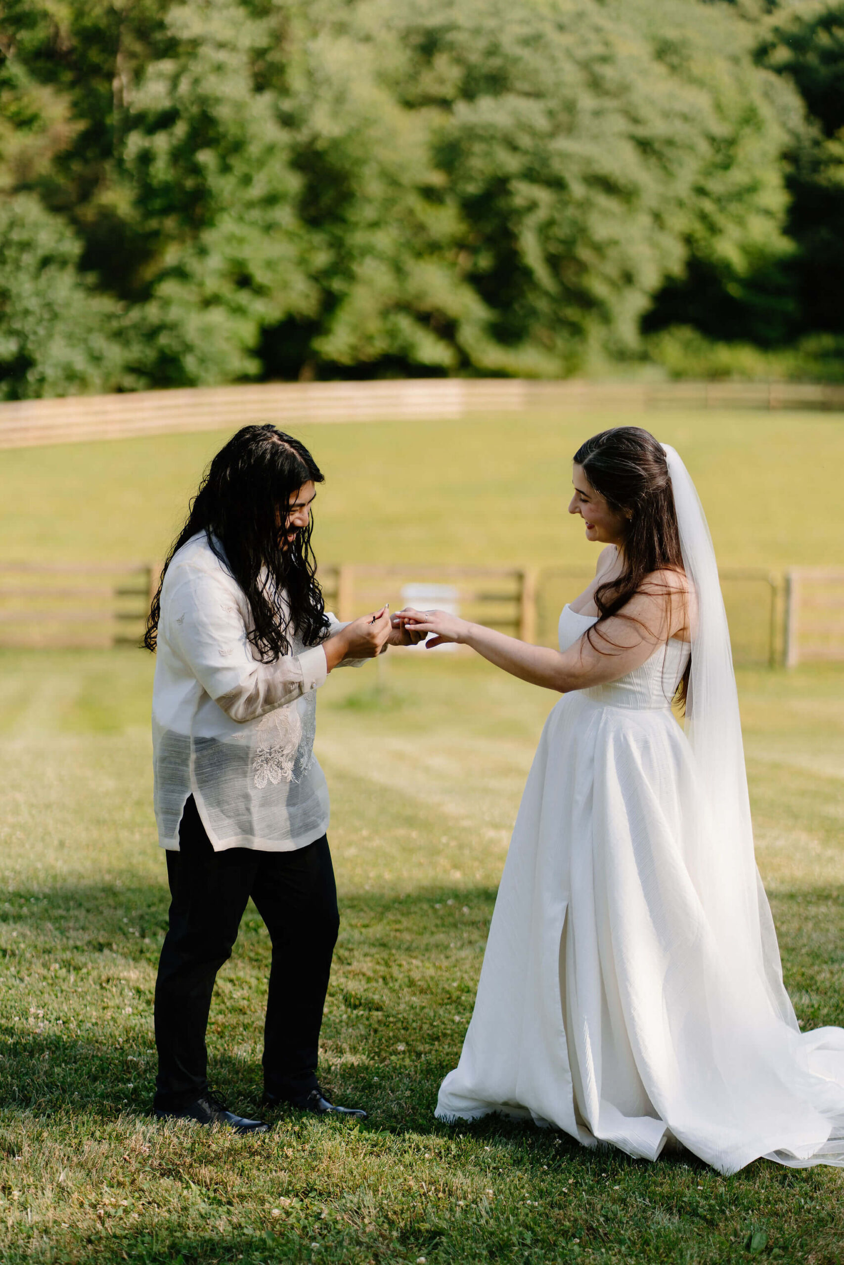 bride and groom standing in an open field on a sunny day exchanging wedding bands