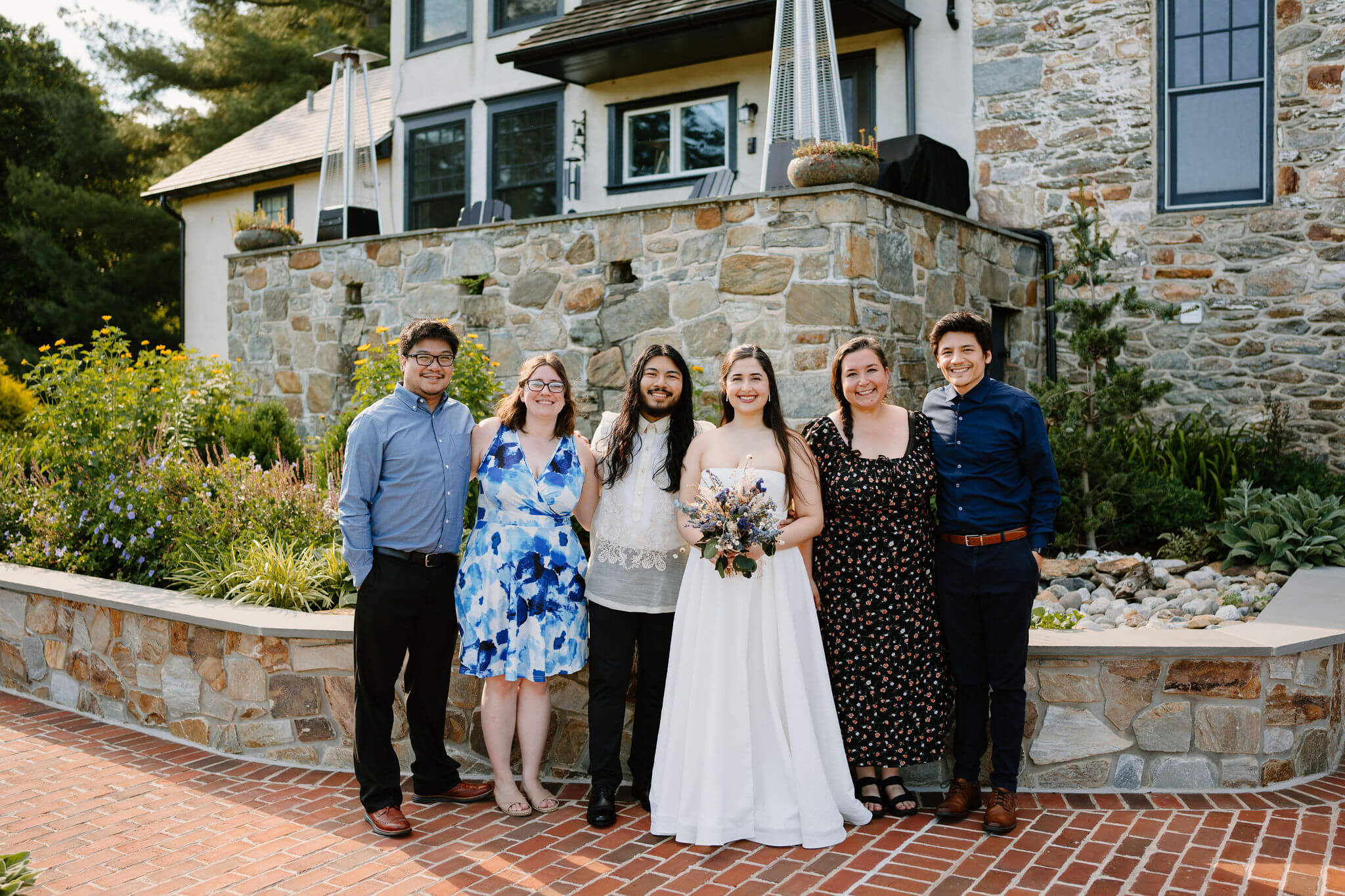 bride, groom, and four of their friends standing together and smiling toward the camera in front of a large stone garden and farmhouse in Pennsylvania