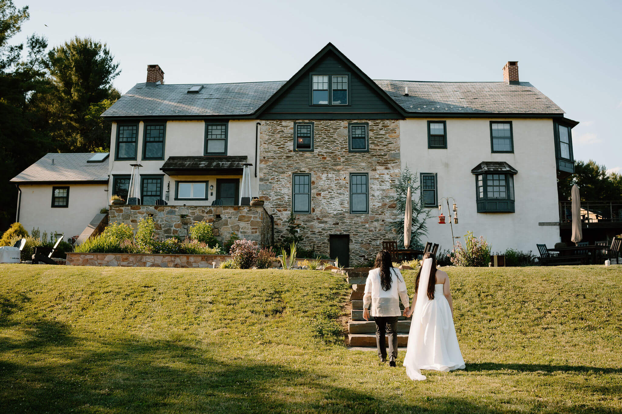 bride and groom holding hands after eloping and walking up a stone path toward a large stone farmhouse in Pennsylvania, away from camera