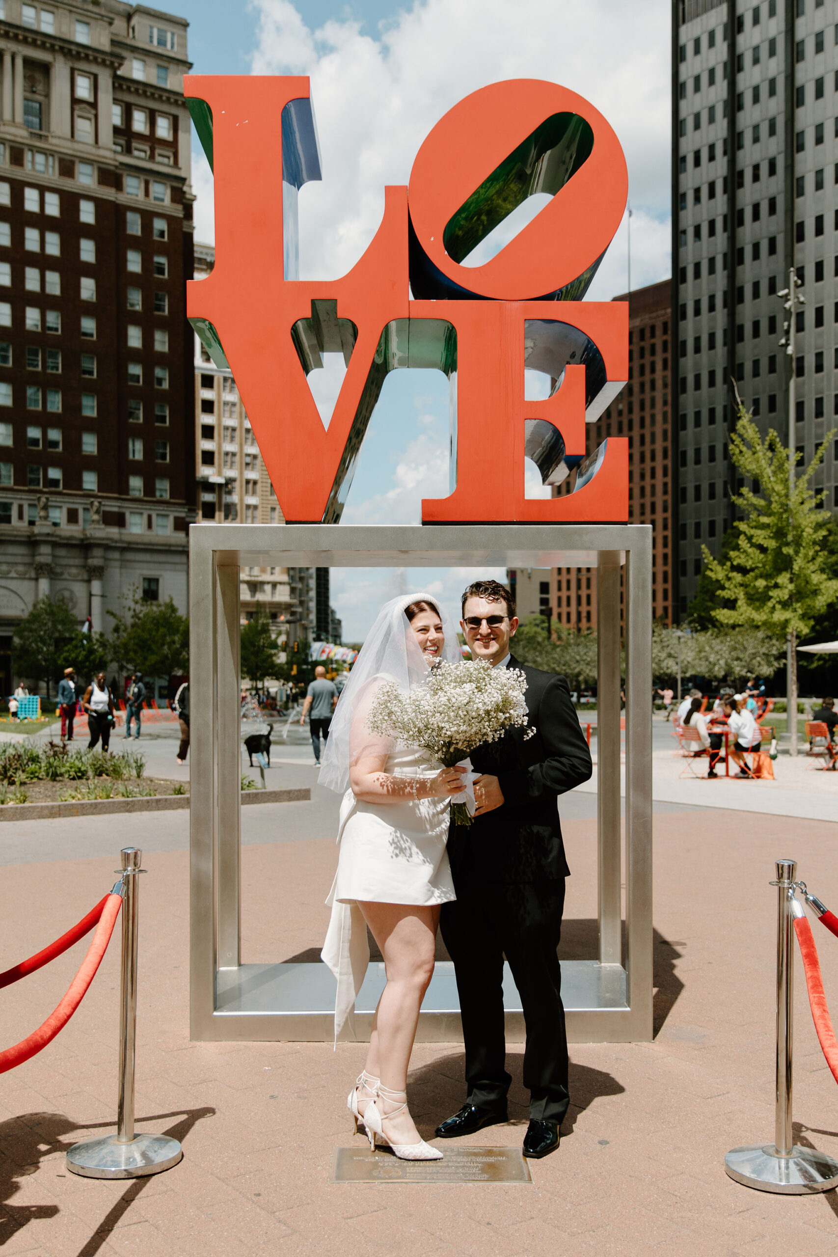 bride and groom smiling toward their guests, bride holding her bouquet after eloping in front of the Love Park sign