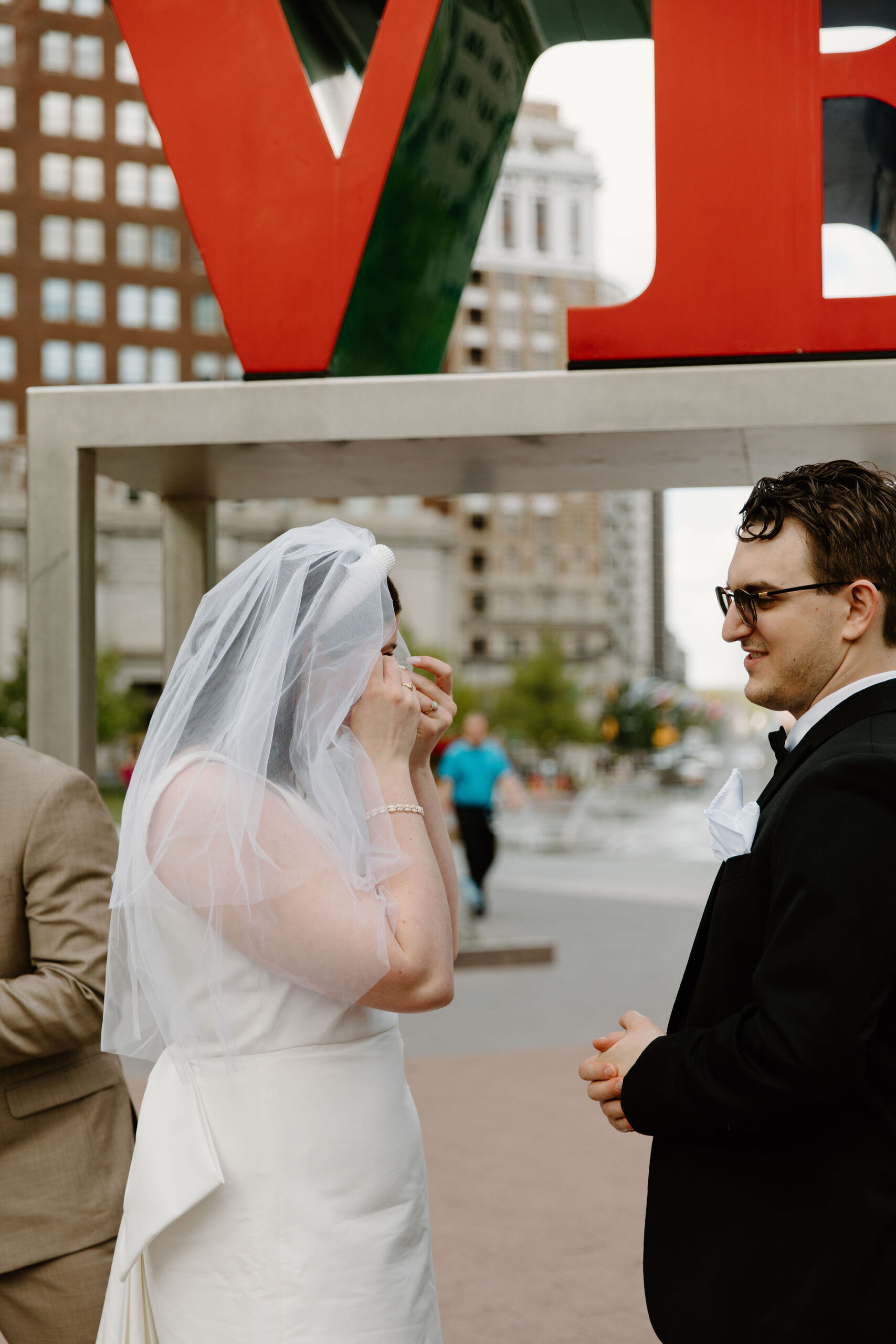 bride crying and dabbing her eyes with a tissue during elopement ceremony at Love Park, while groom stands next to her 