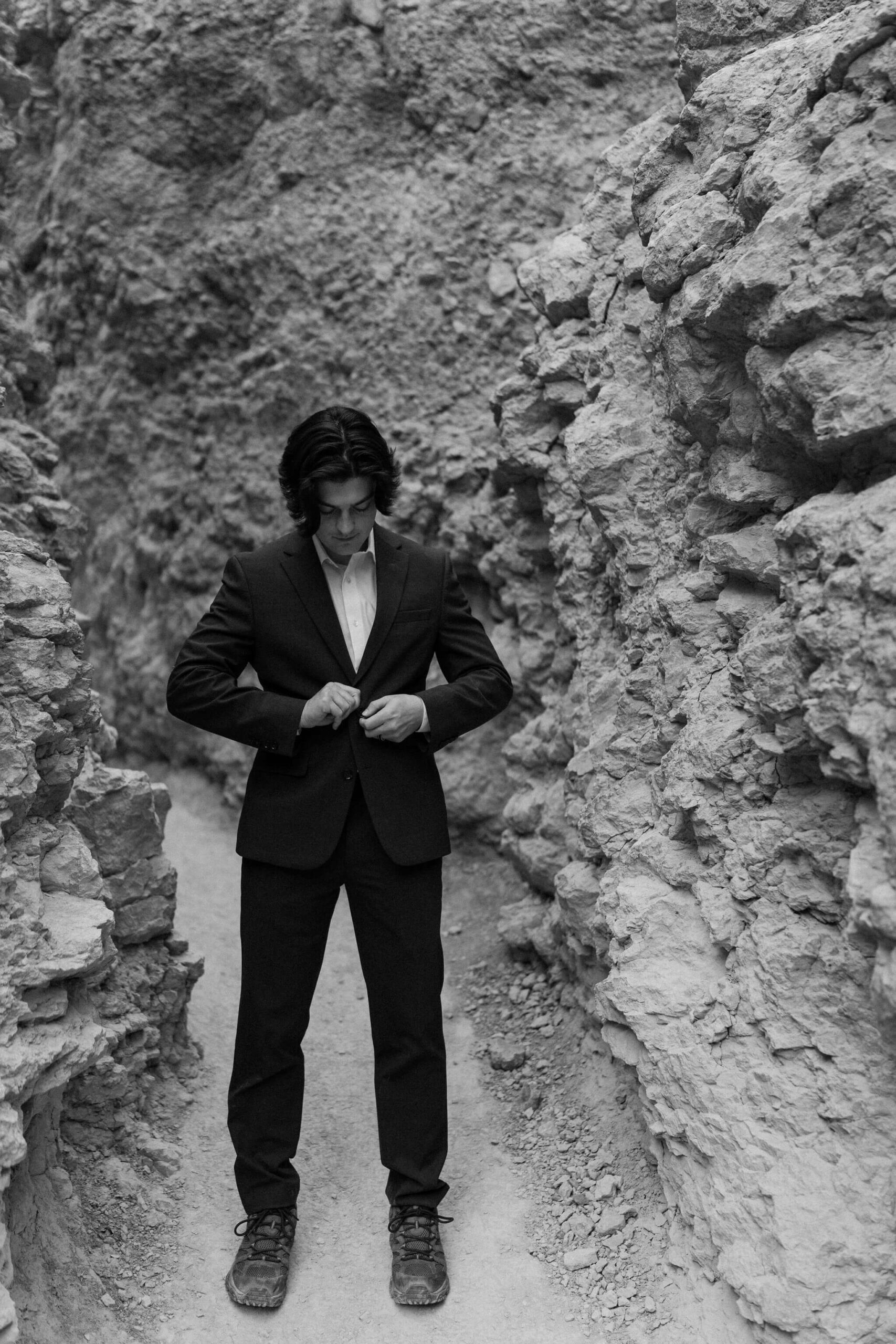groom on a narrow trail surrounded by tall red rocks, buttoning his suit jacket