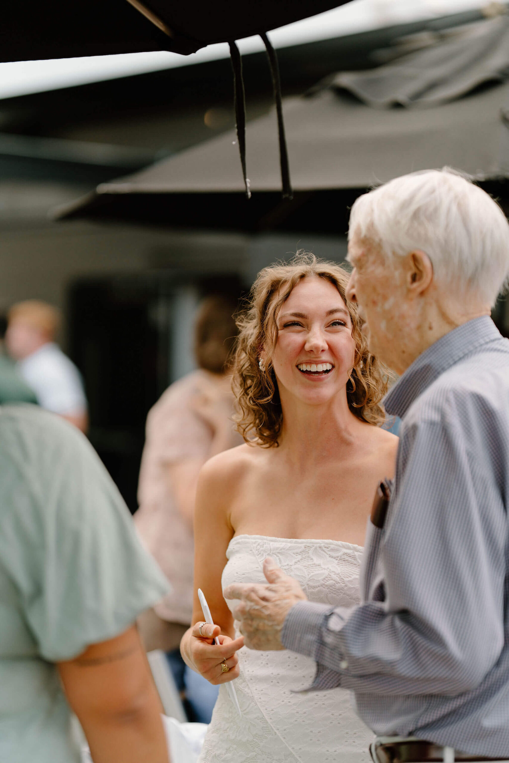 bride (strapless lacy dress) smiling and laughing while talking with her grandfather