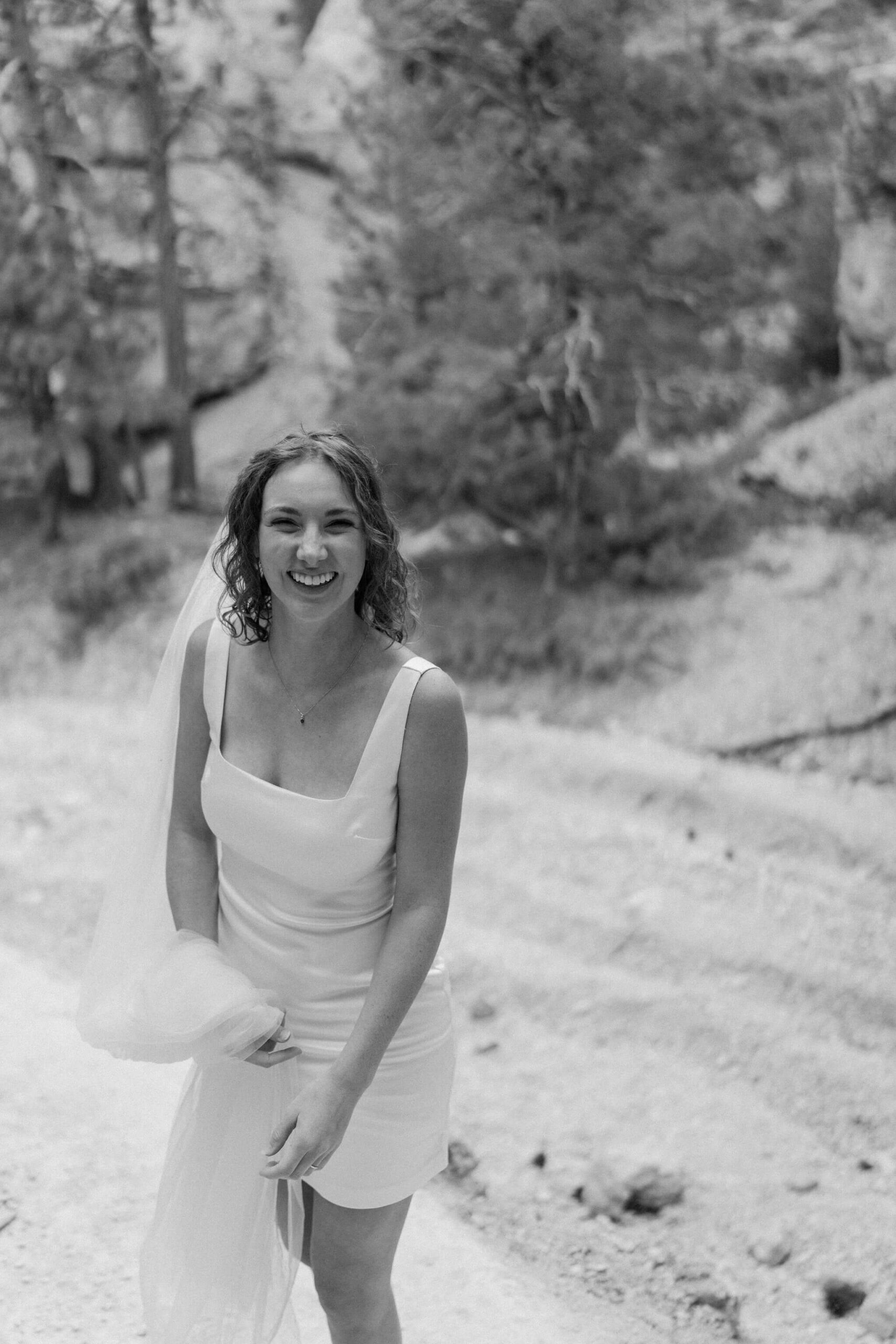 black and white image of a bride in a short wedding dress, holding up her long veil and laughing