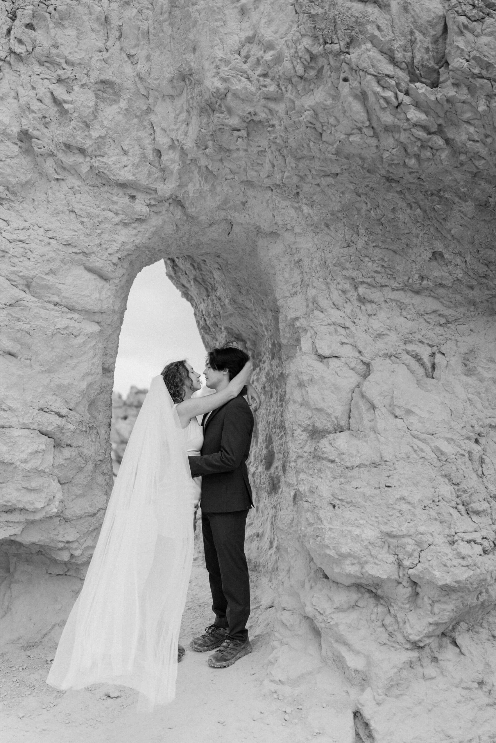 bride and groom embracing in front of a small archway through a wall of red walks