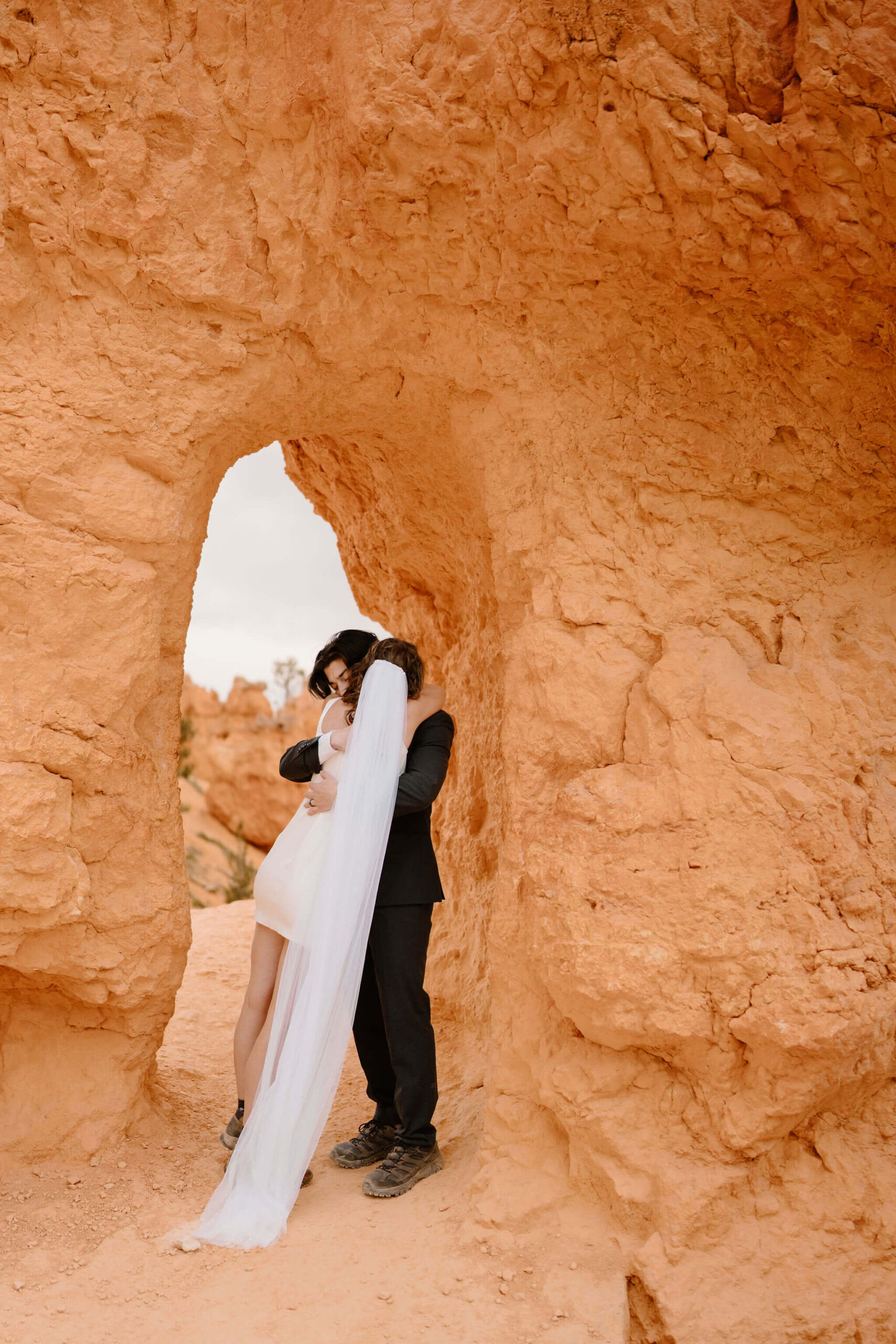 bride and groom embracing in front of a small archway through a wall of red walks