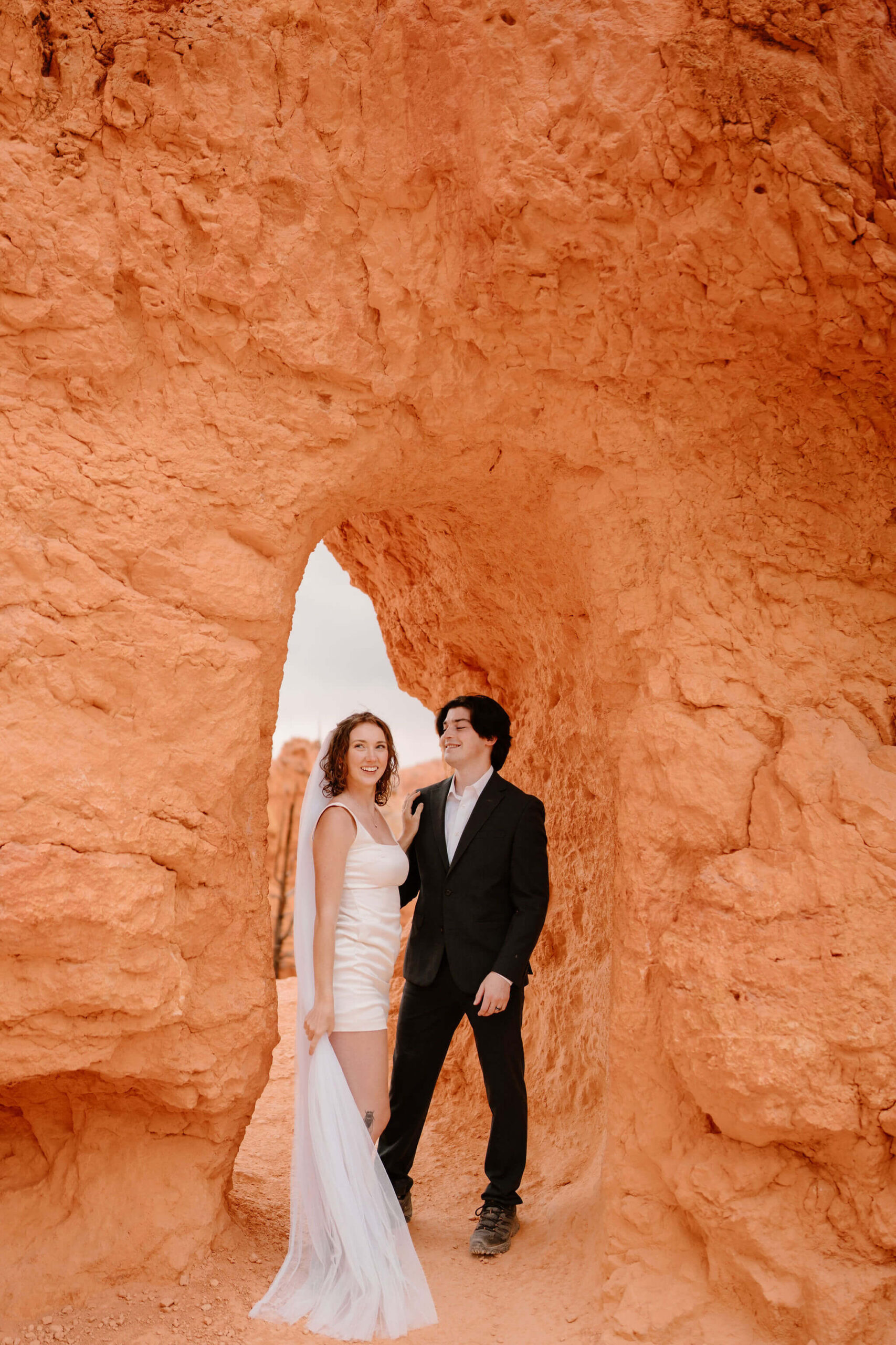 bride and groom embracing in front of a small archway through a wall of red walks