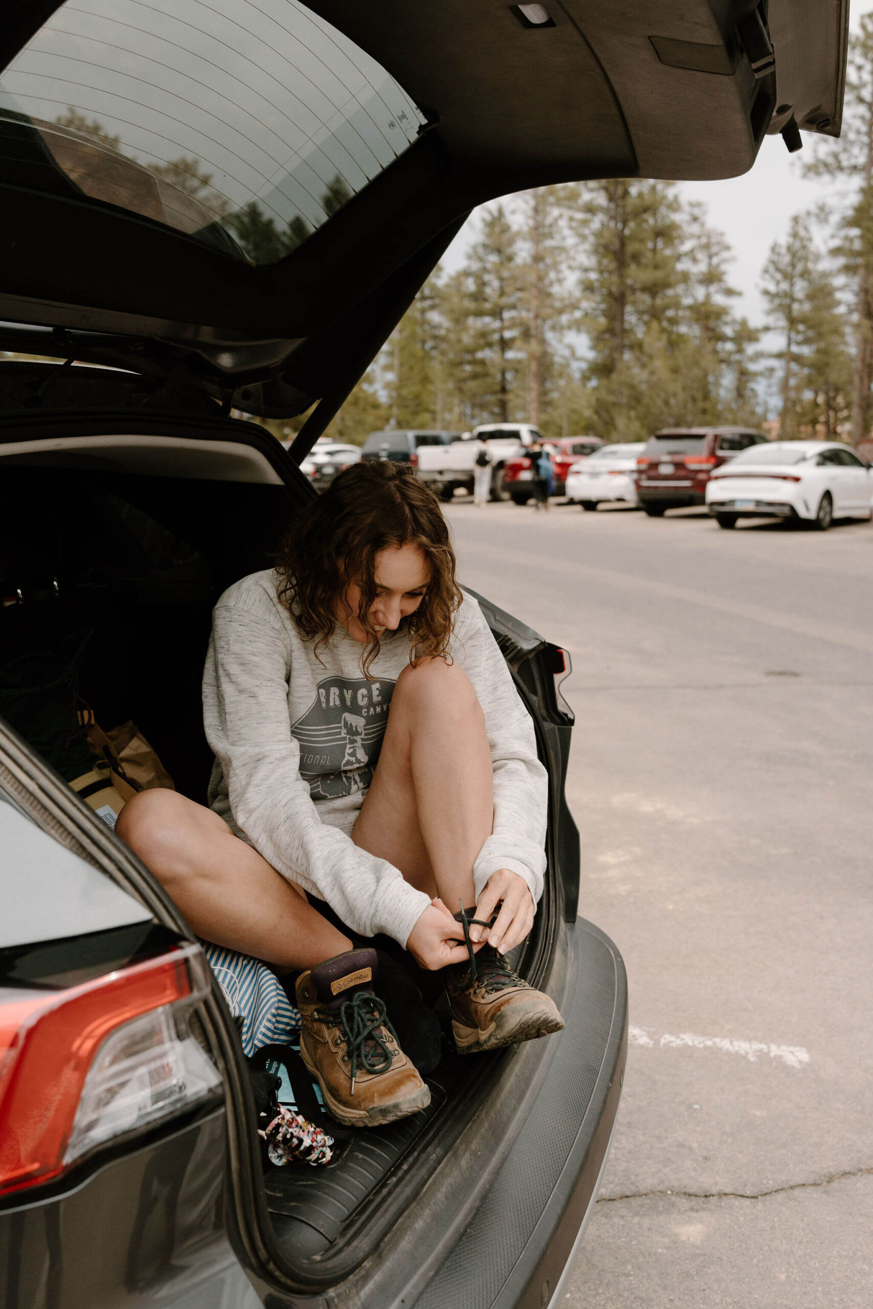 woman lacing her hiking boots and smiling, in the open trunk of an SUV