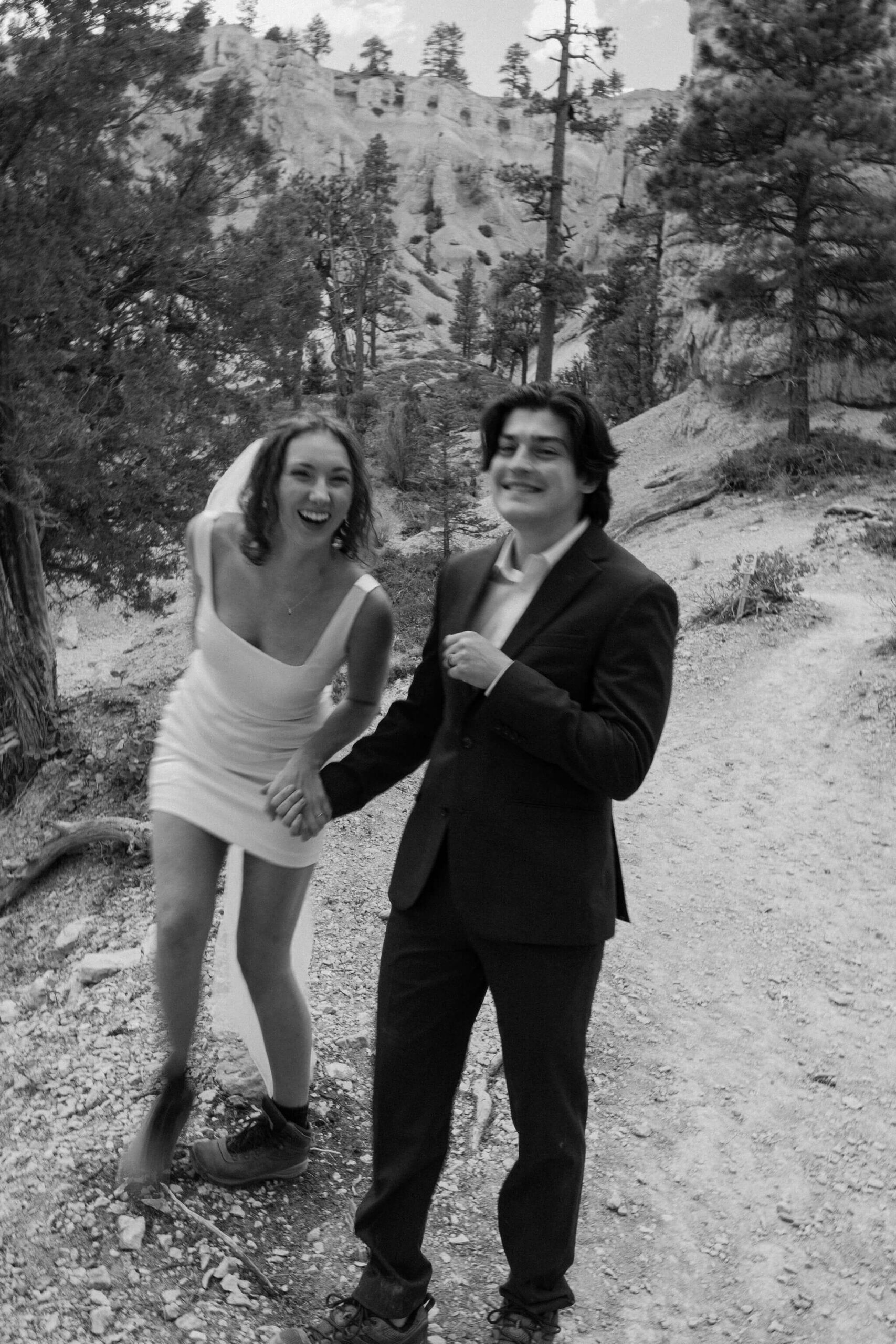 black and white image of bride and groom laughing and smiling while holding hands