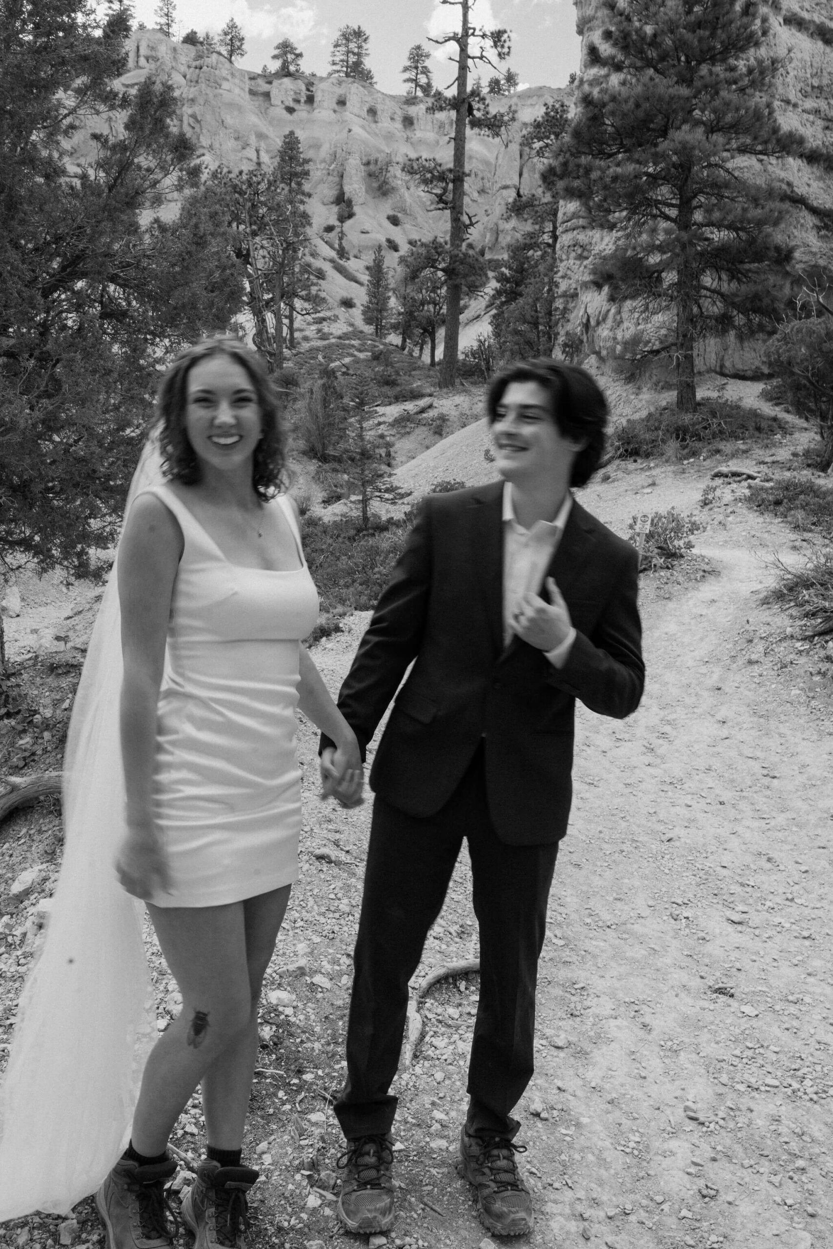 black and white image of bride and groom laughing and smiling while holding hands